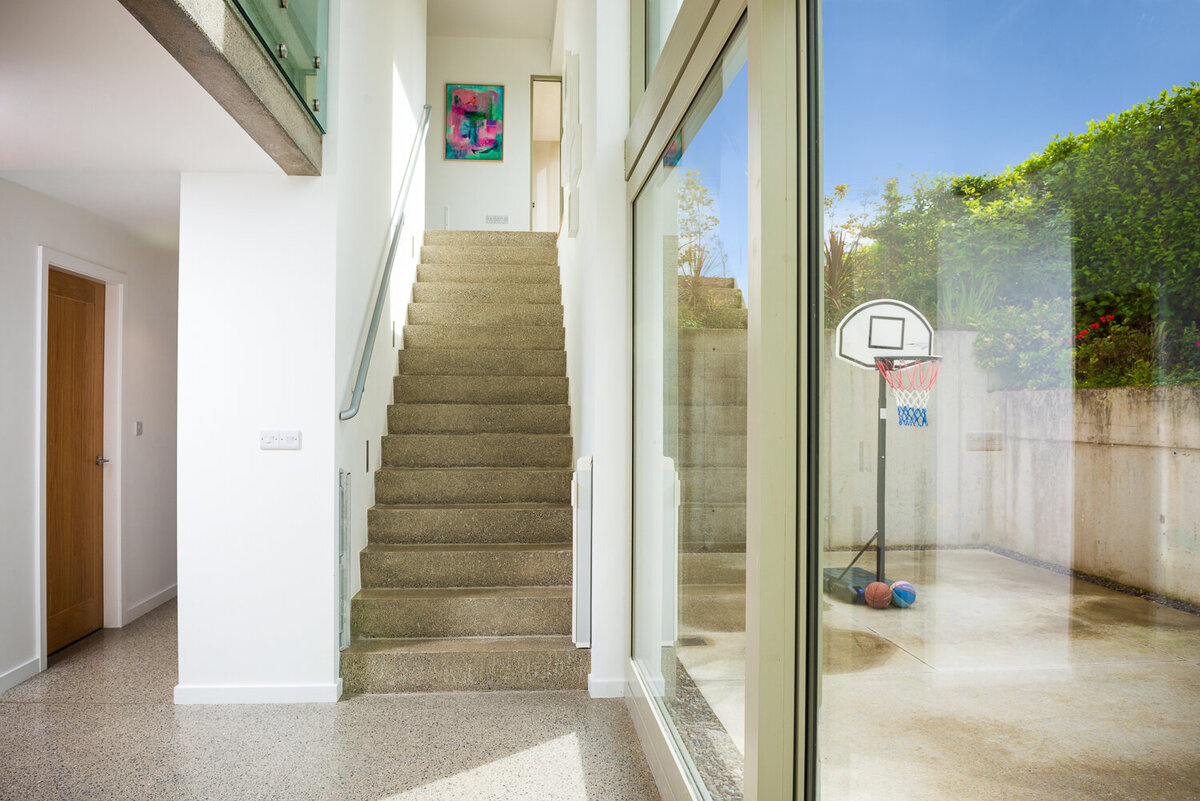 Architect designed house below level with concrete floor and stairs with ceiling height glass