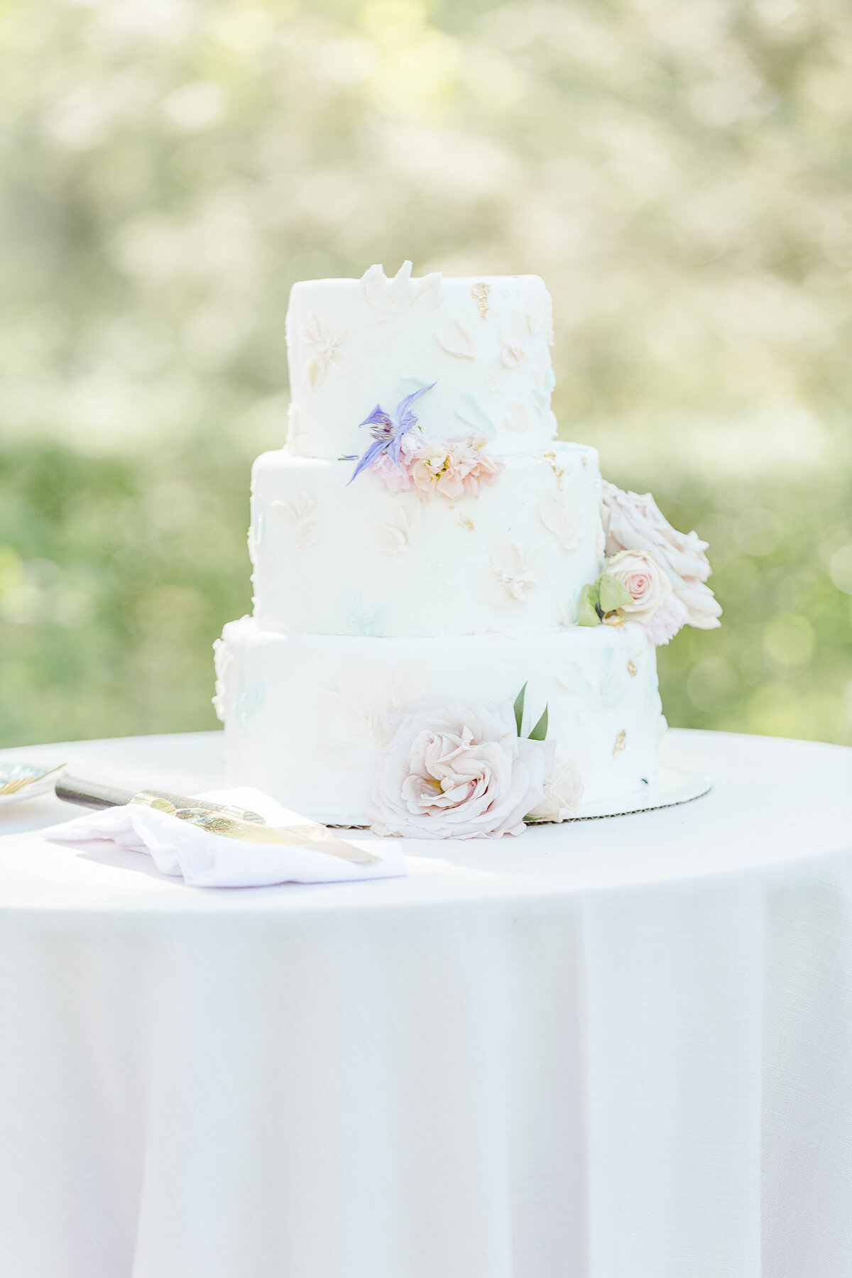 White wedding cake is displayed at an outdoor french-inspired wedding. Captured by best Massachusetts wedding photographer Lia Rose Weddings