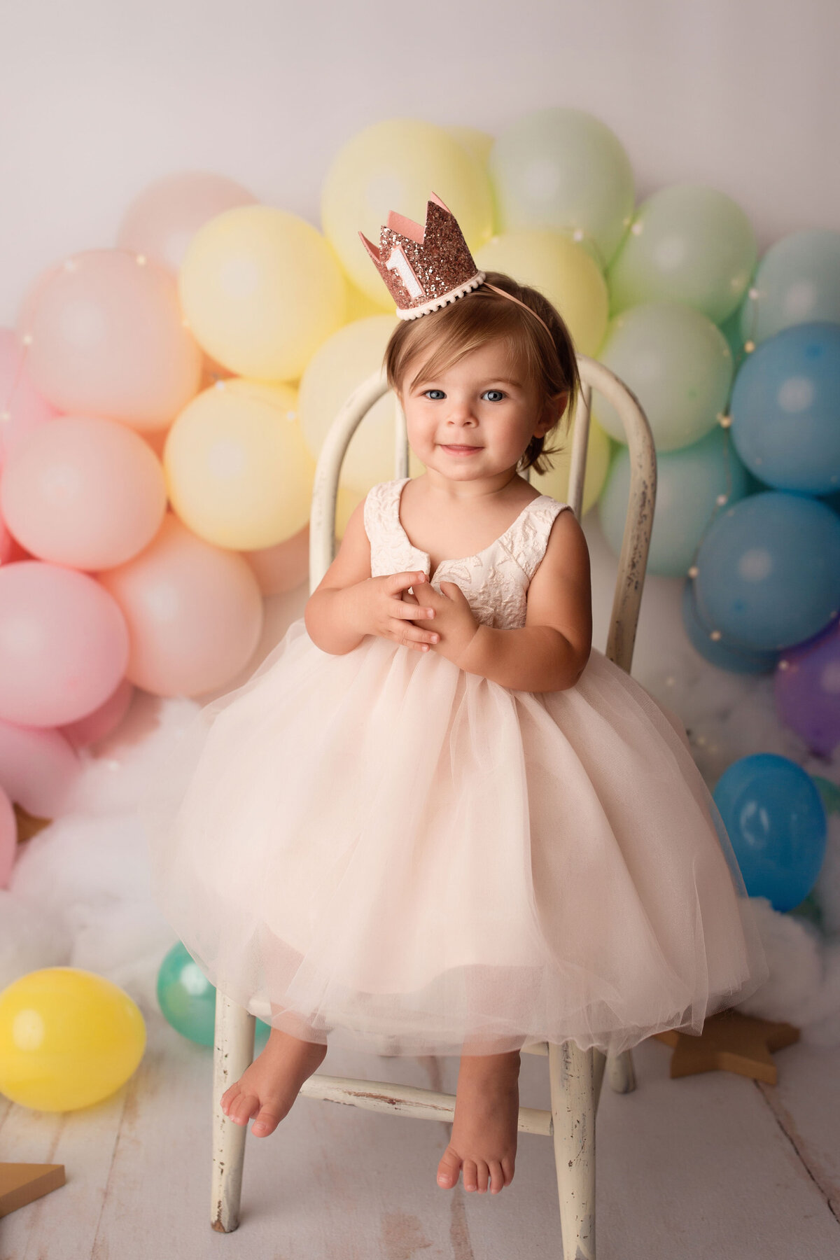 birthday girl wearing a pink dress with rainbow balloons behind her
