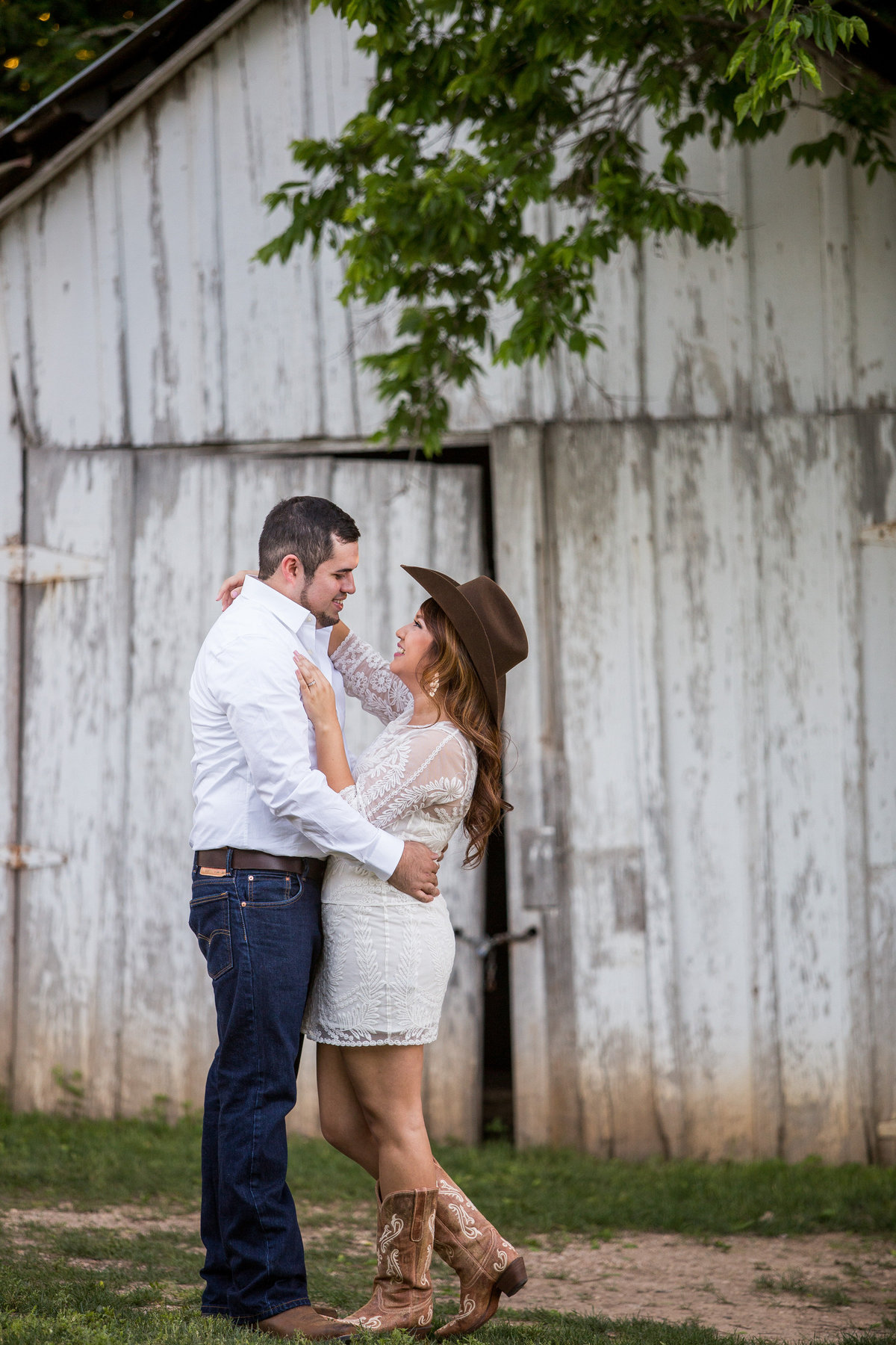 Engagement session a Gruene where woman wears her fiancé's cowboy hat and lifts her leg.