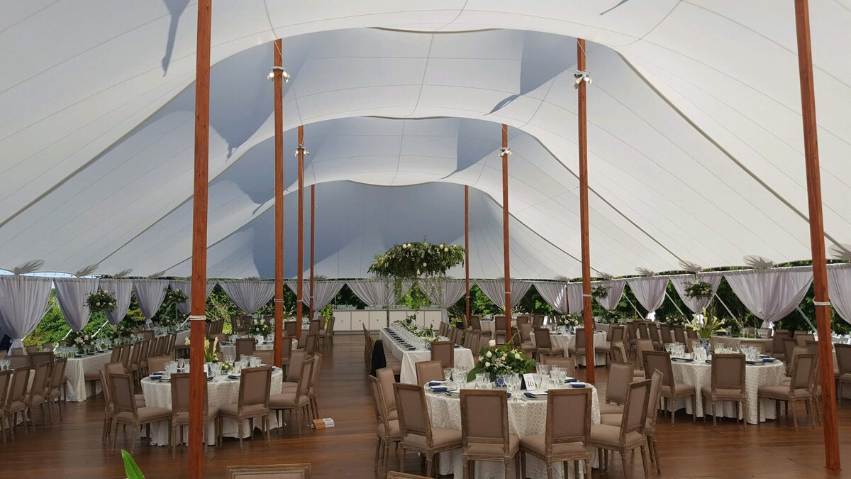 The inside of a stunning pole marquee set for a wedding breakfast with beautiful linens with a mix of low and high floral arrangements.