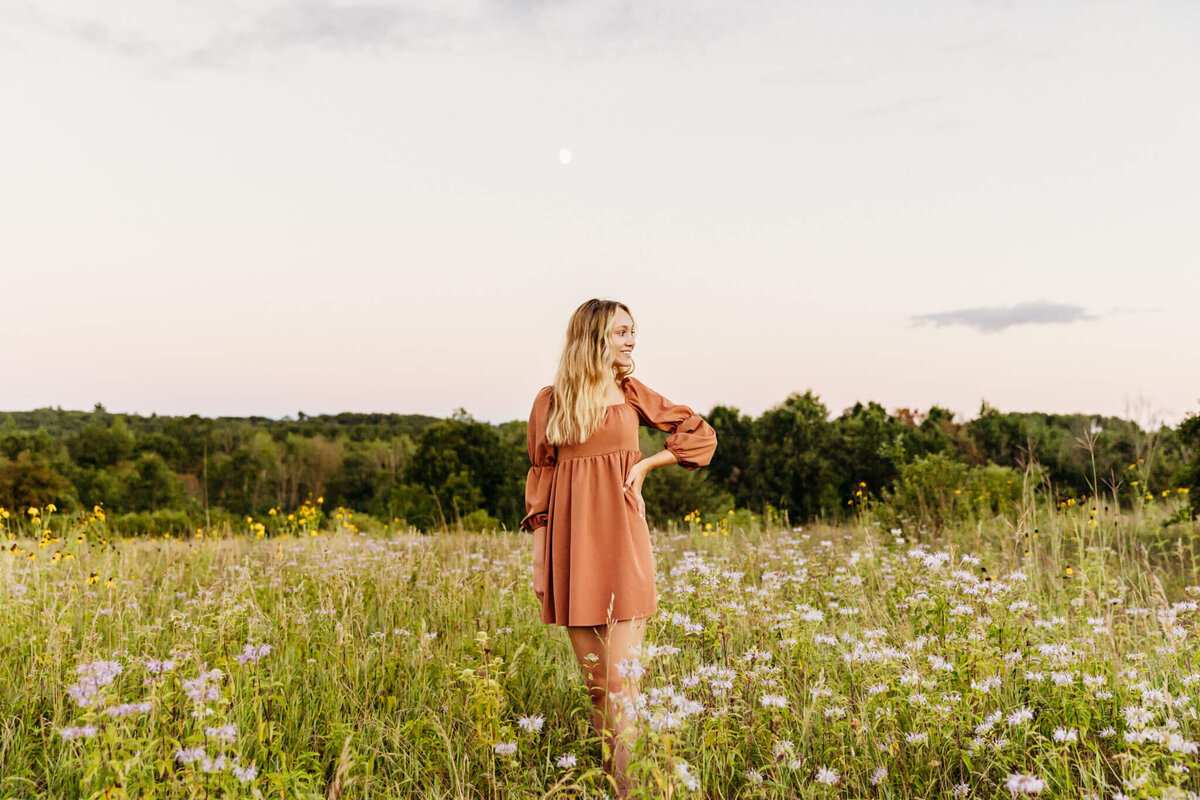 blonde girl teenager in an orange dress posing in a field of wildflowers for her senior photos