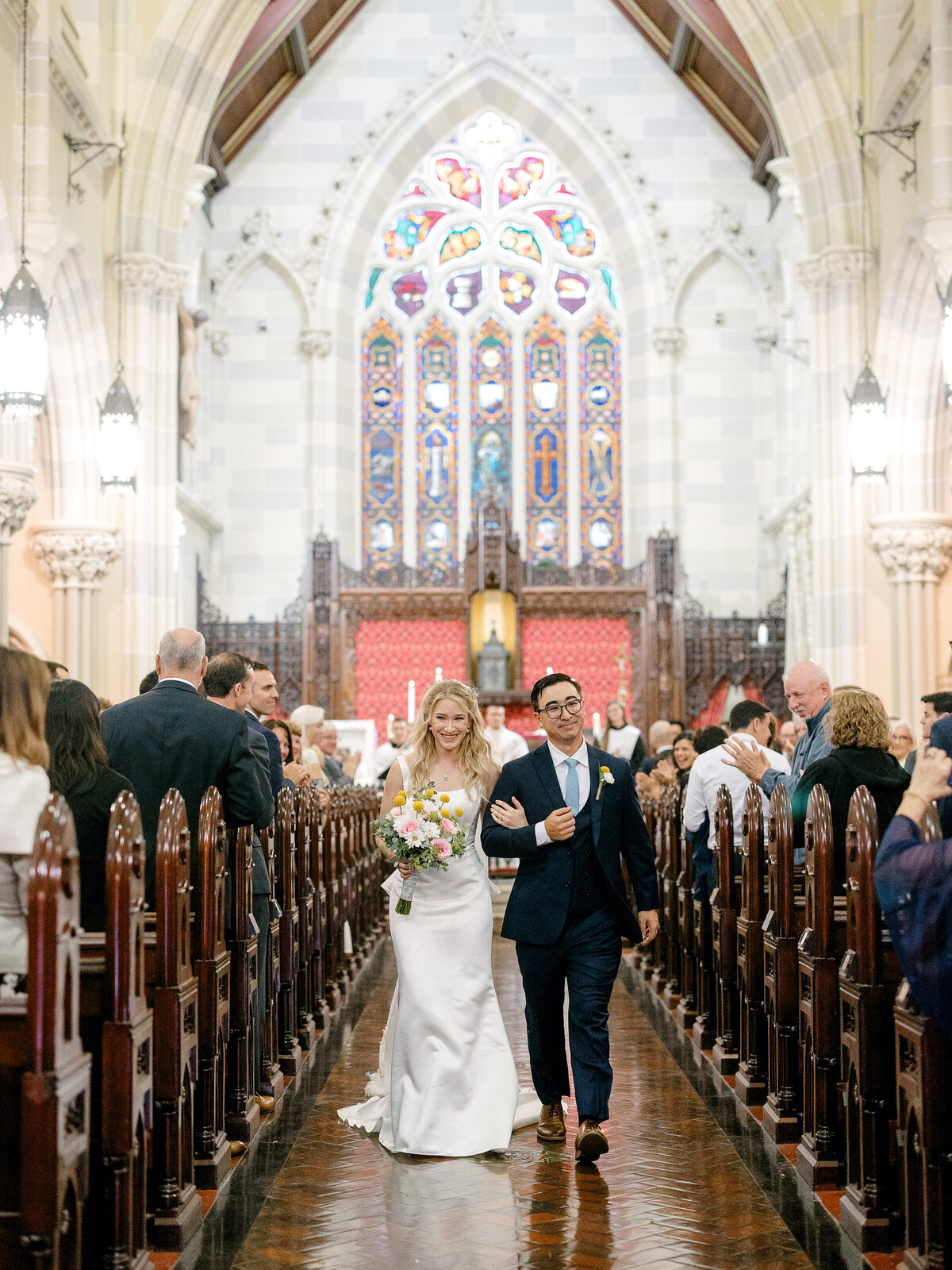 Bride and groom walking back down the aisle in an ornate church with stained glass windows