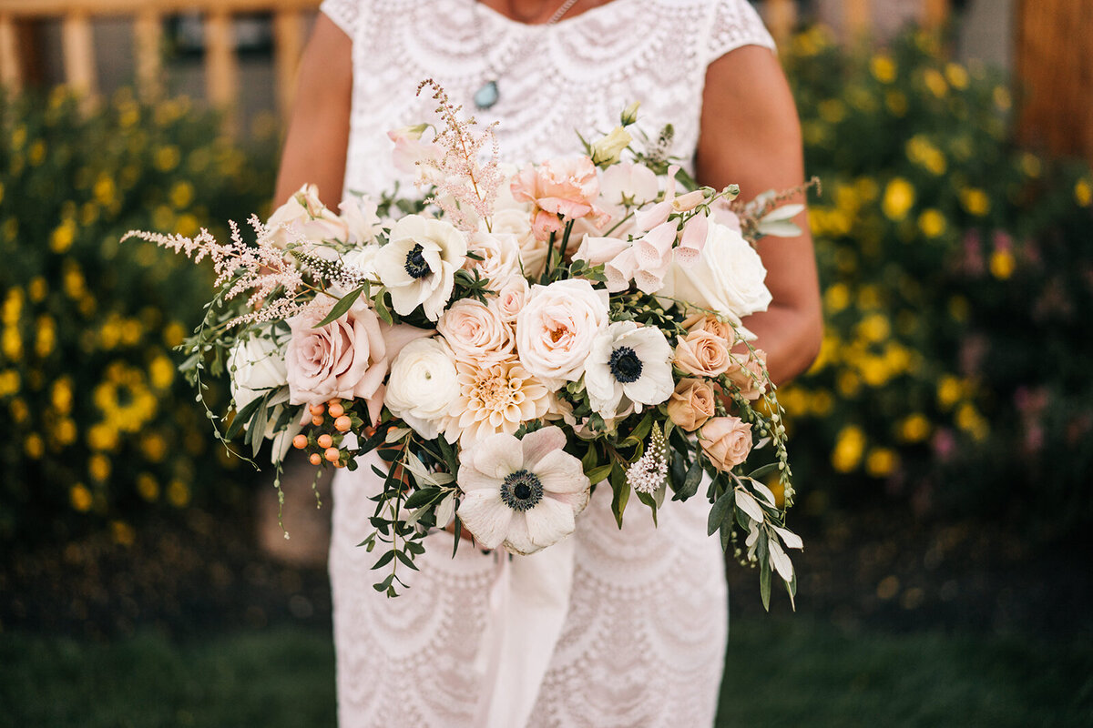 Bride holding blush bouquet with anemones, roses, ranunculus and dalhlias