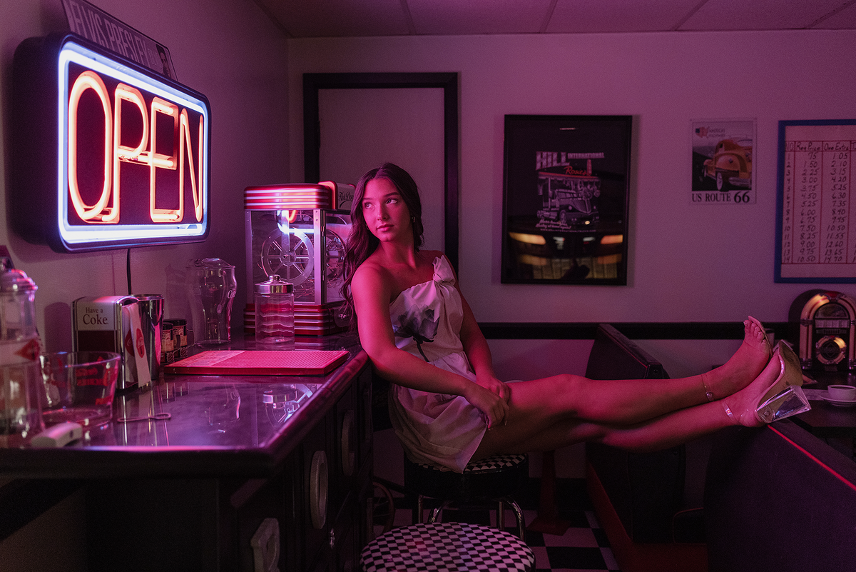 Senior girl sitting in oldies diner with neon light on