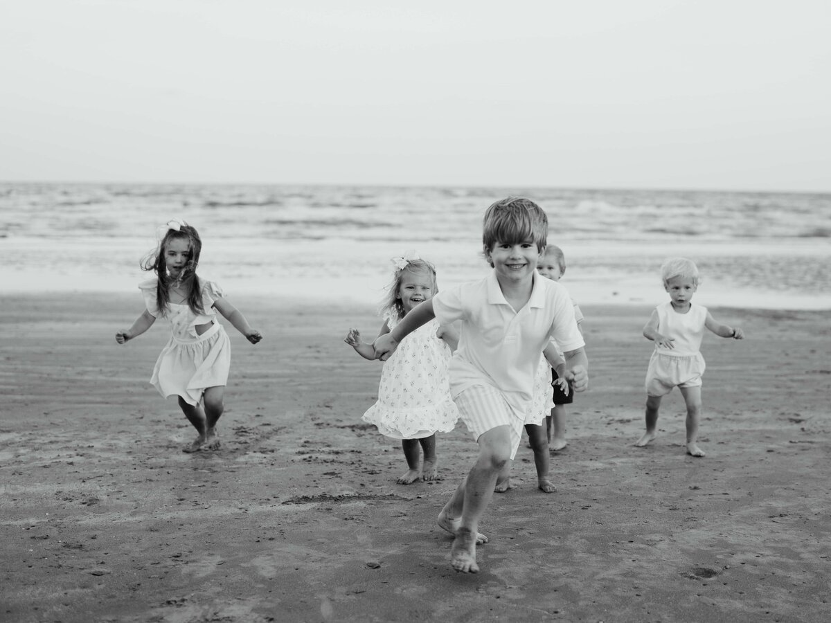 Children gleefully running towards camera at the beach in black and white