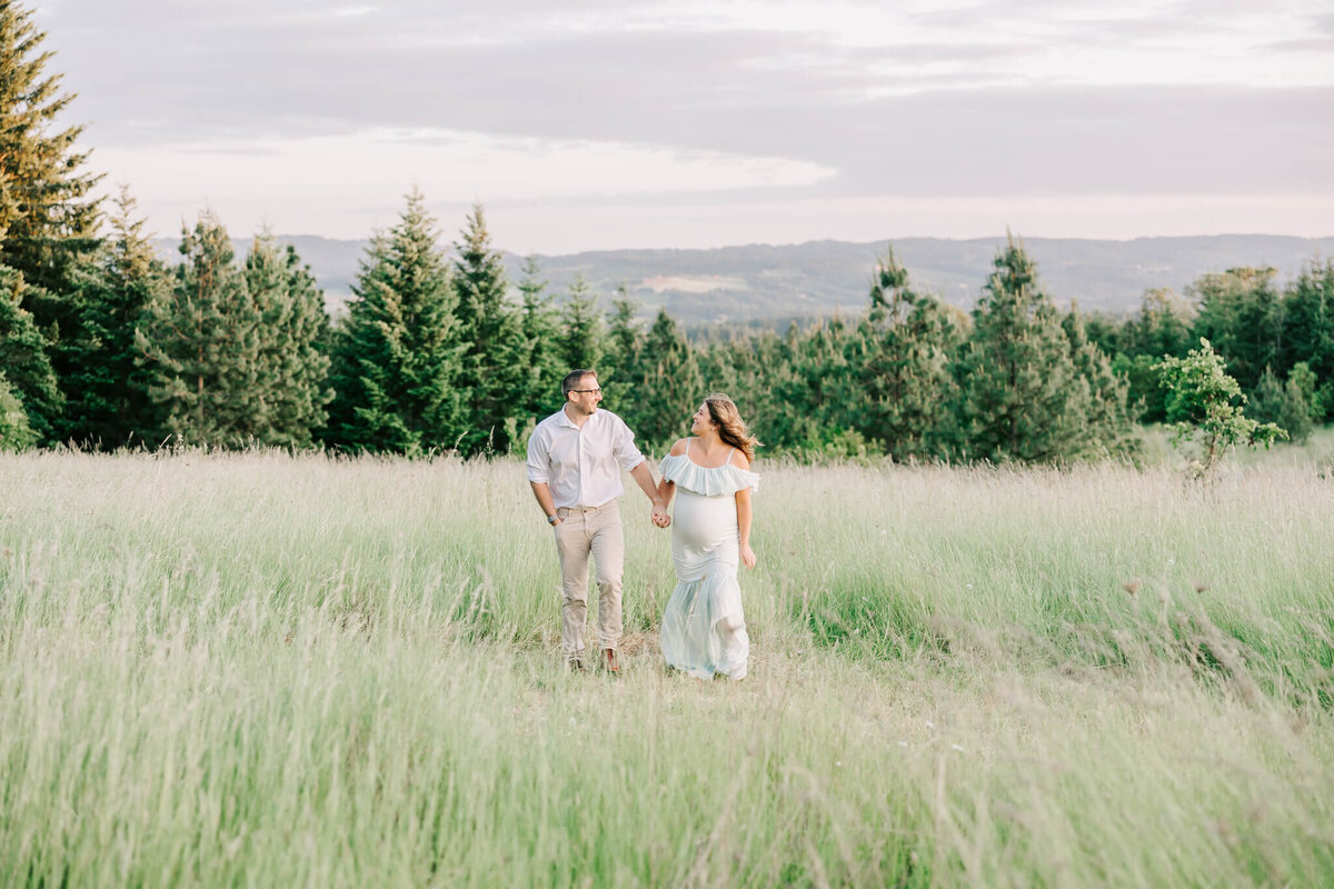 portrait of a couple walking in a field and holding hands for their maternity photography session in portland oregon