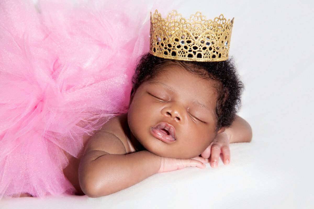 Newborn dressed in pink tutu and wearing a crown sleeps during photo session