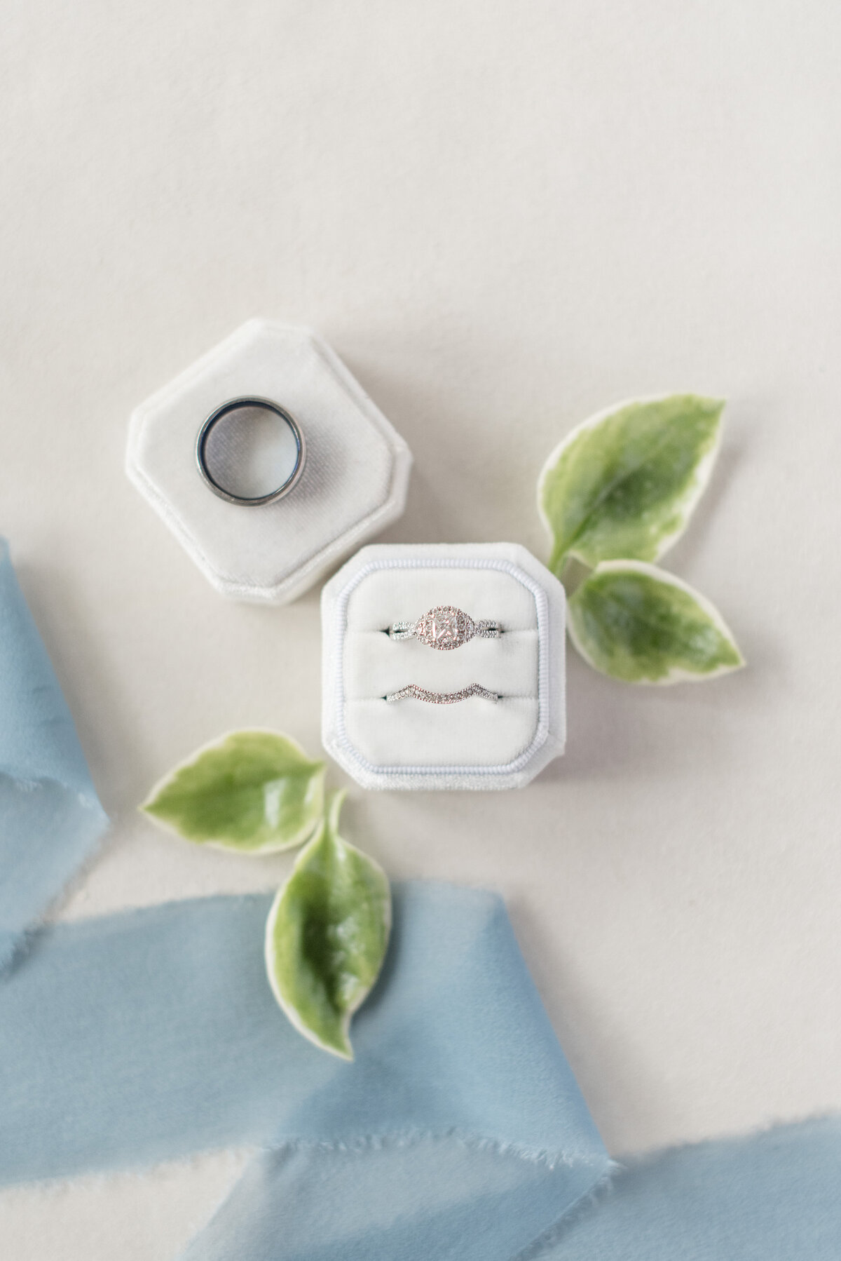 Diamond wedding rings inside white box with dark gray wedding band resting on box lid.