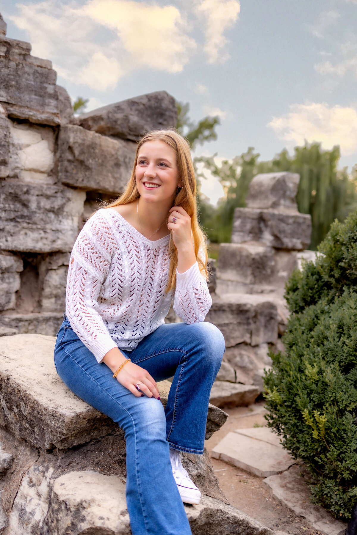 A girl is casually sitting on the ruins in Tower Grove Park and looking over her shoulder to the right while smiling big for her senior photo session.