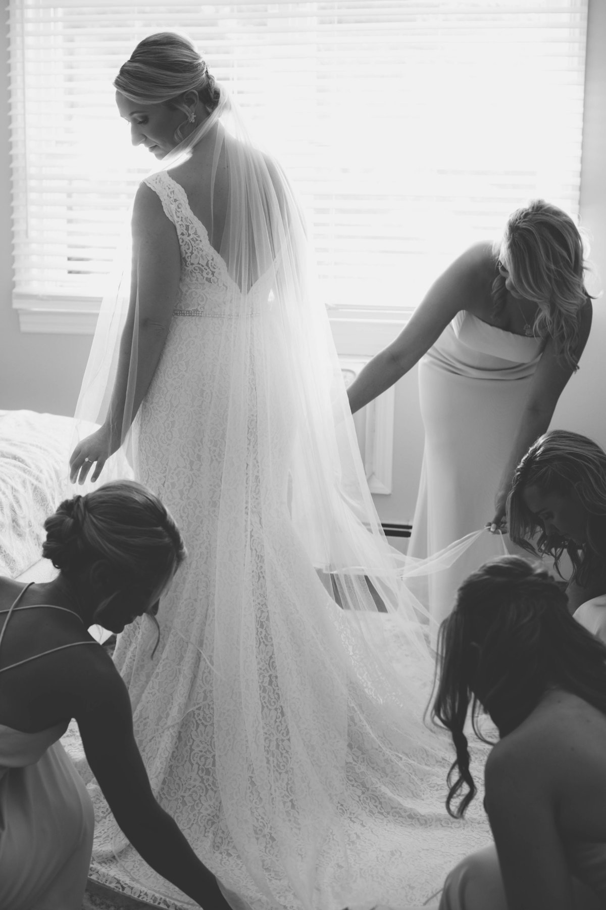 bridesmaid helping bride with dress in black and white photo from wedding at The Mansion at Timber Point