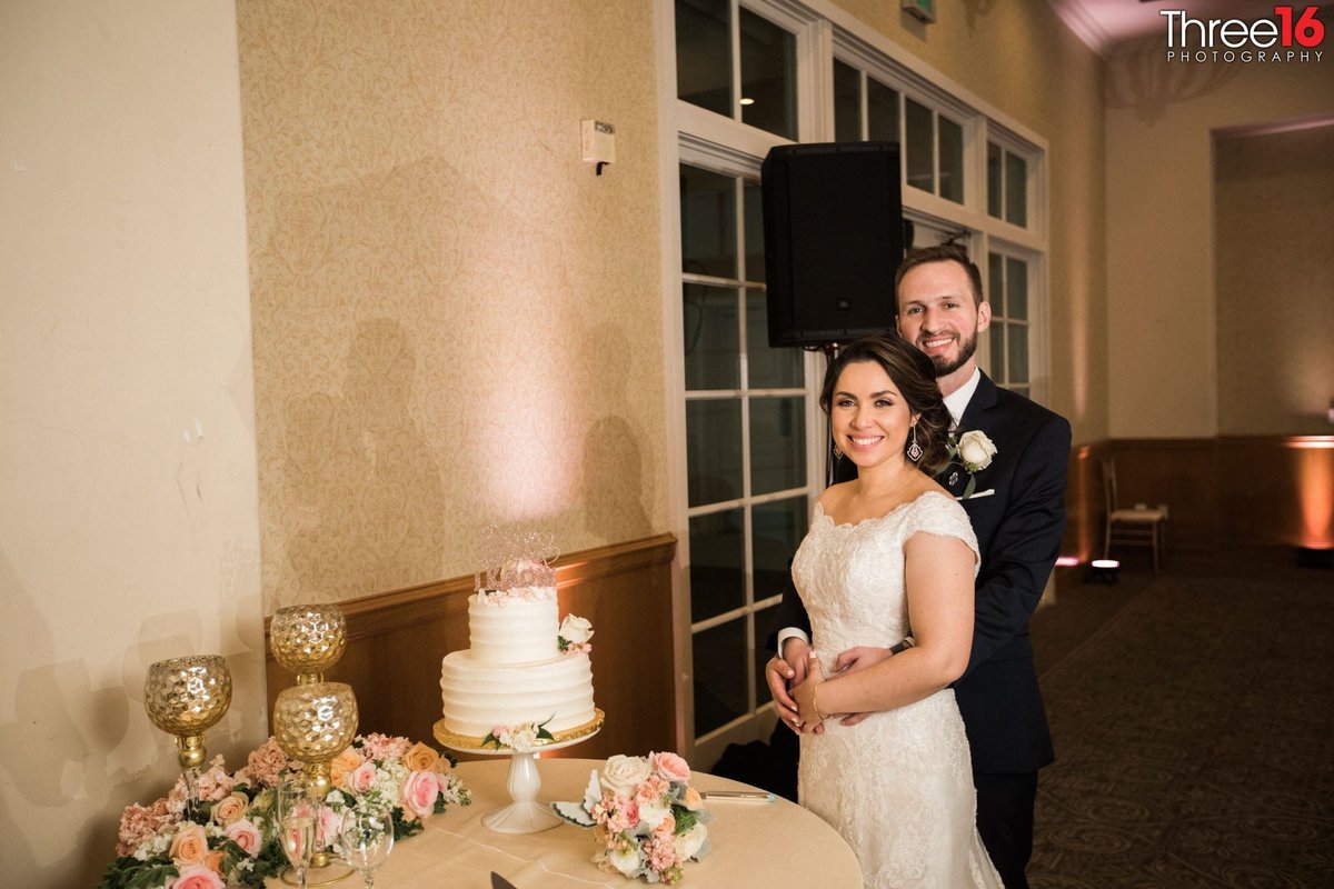 Bride and Groom pose next to their 2-tiered white wedding cake