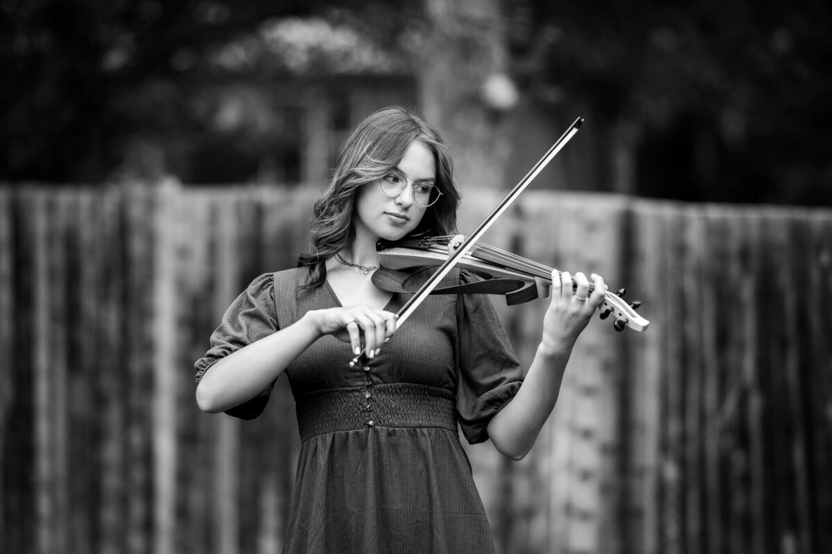 black and white image of a teenage girl  playing her violin outside