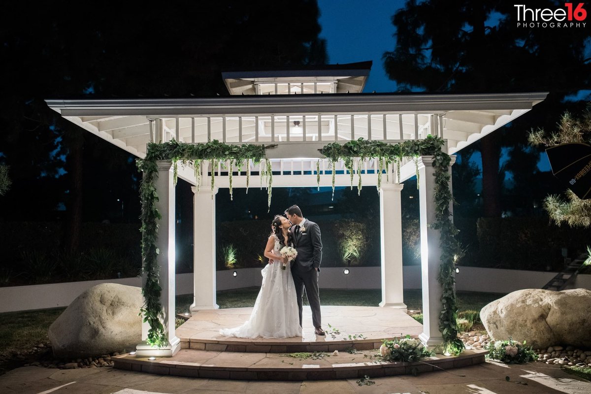 Married couple kiss at night under the lighted gazebo