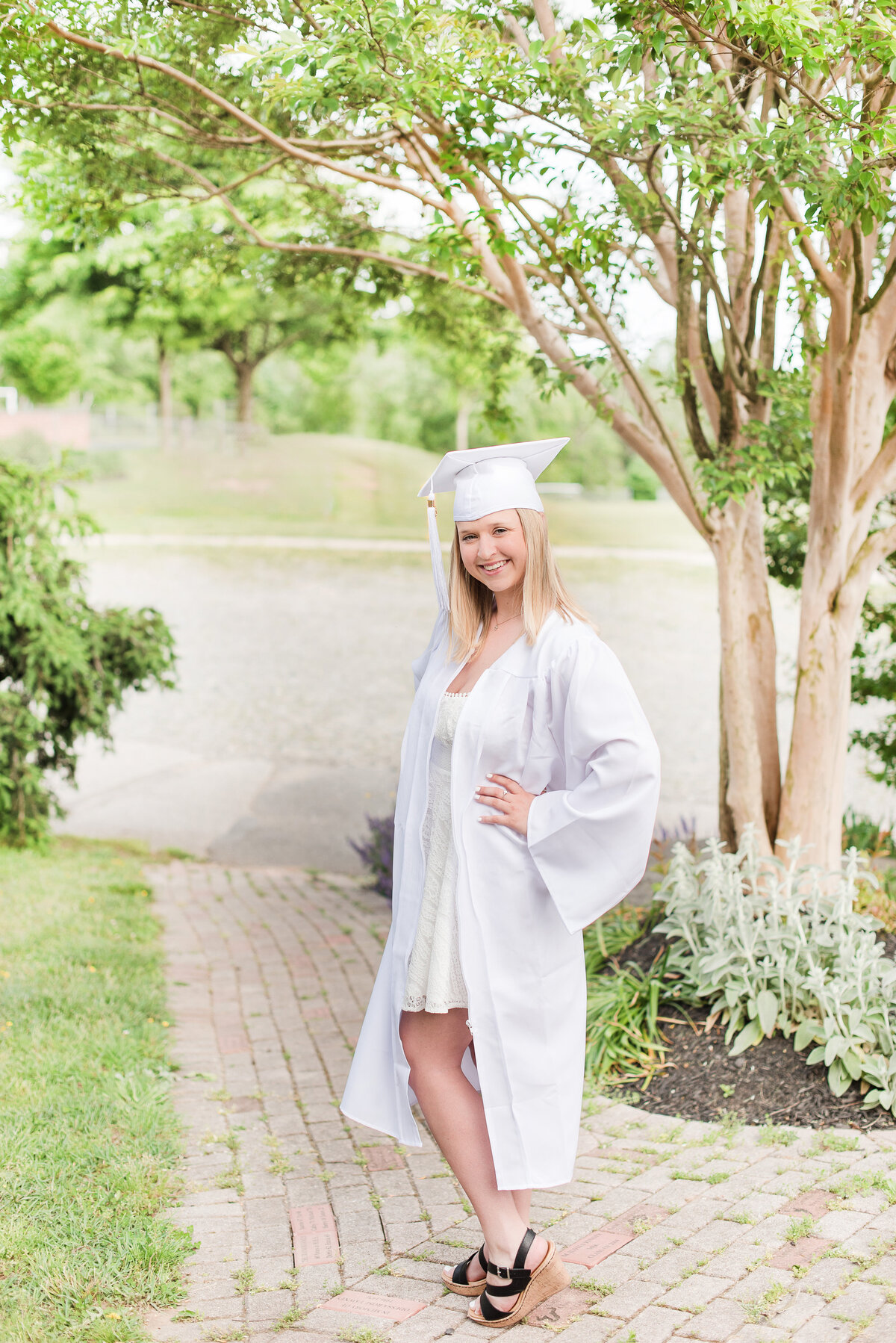 high school senior in white cap and gown on brick sidewalk