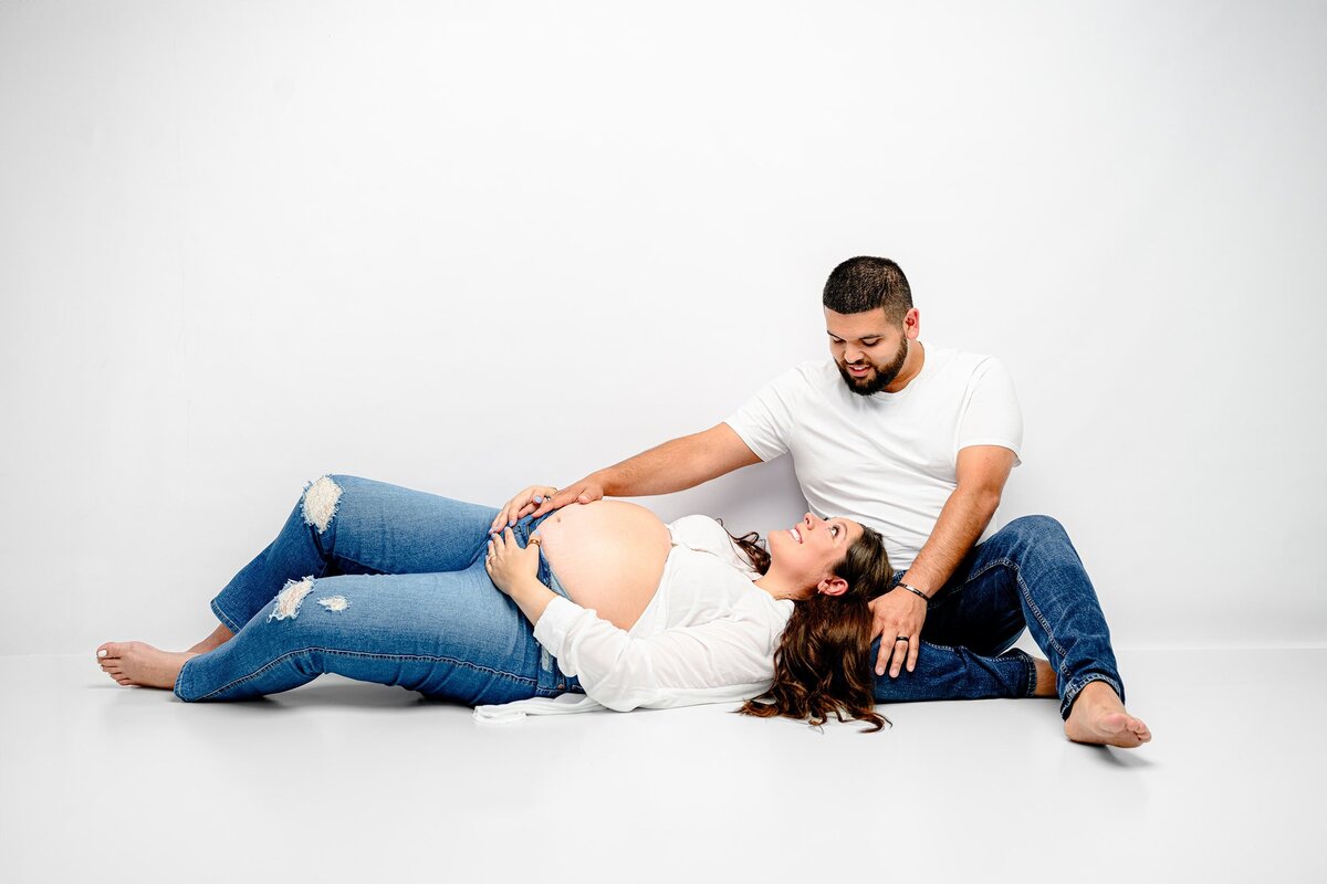 Expectant father sits with his pregnant charlotte area wife's head laying in his lap while he cradles her baby bump