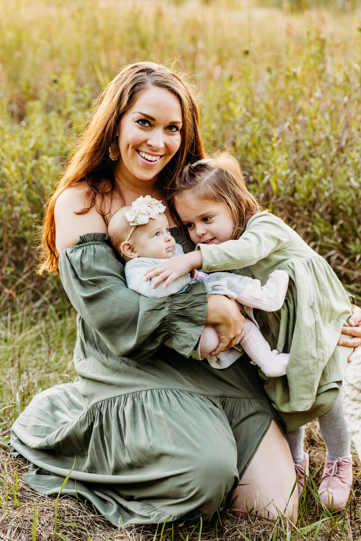 gorgeous mama in green holding her two daughters in her arms as the oldest daughter hugs baby captured by Ashley Kalbus Photography