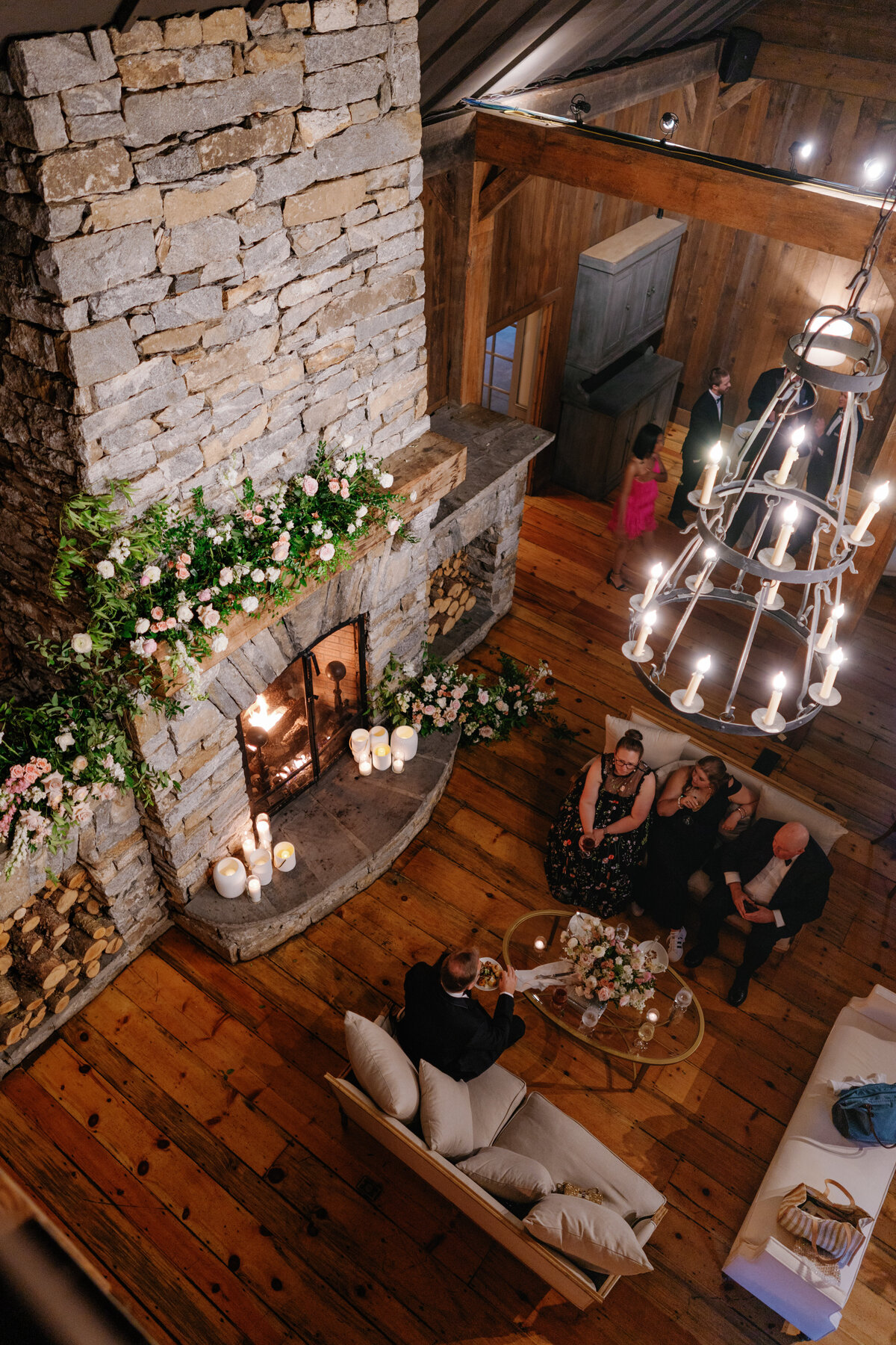 Wedding guests sit and eat cake next to the grand fire place at Farm at Old Edwards summer destination wedding.