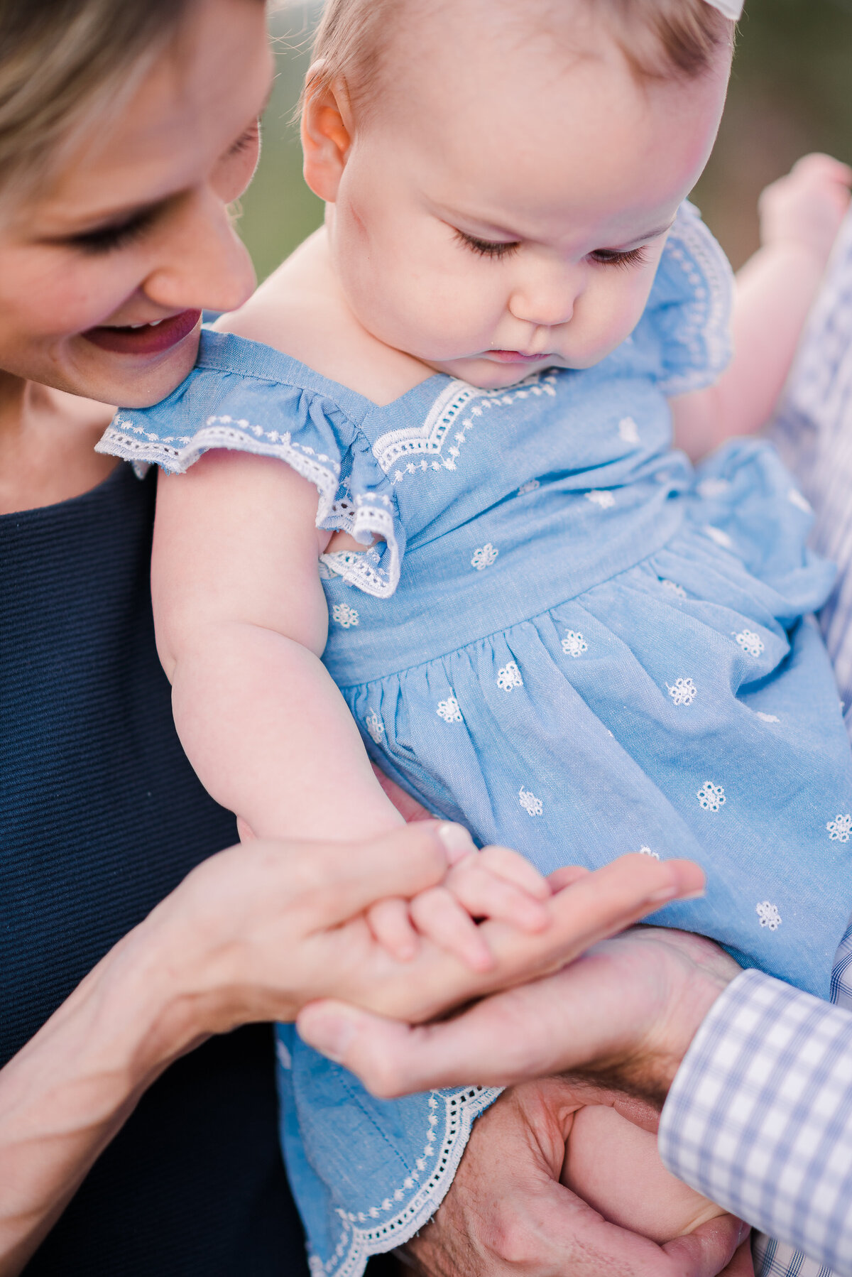 detail photo of mom and dad holding their daughters hand as she wear a a light blue denim dress photographed by denver family photographers