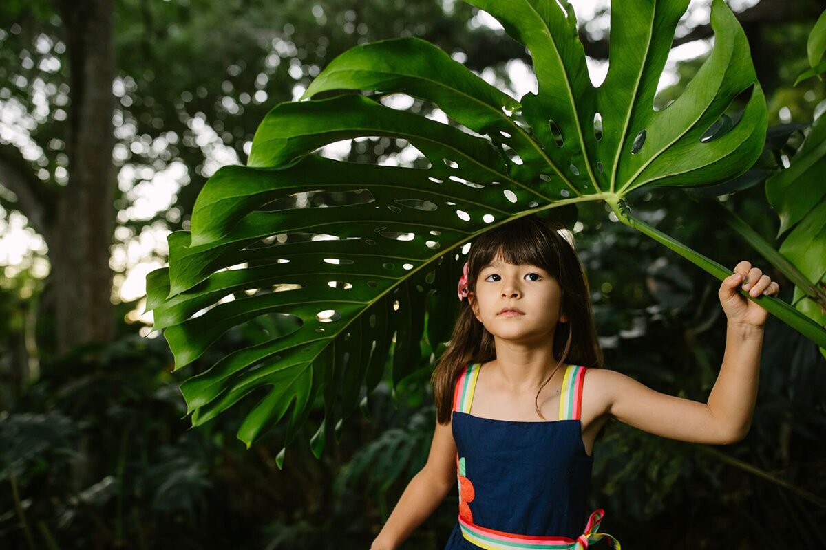girl poses under a large monstera leaf in hawaii