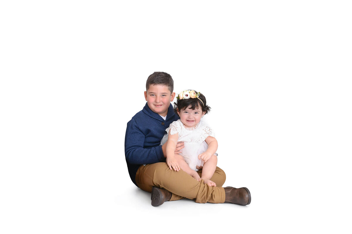 siblings smile at their camera in front of a white background at their photoshoot