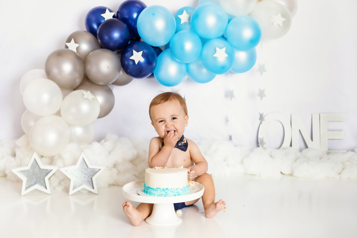 Cake Smash Photographer, a baby boy eats cake before balloons during first birthday