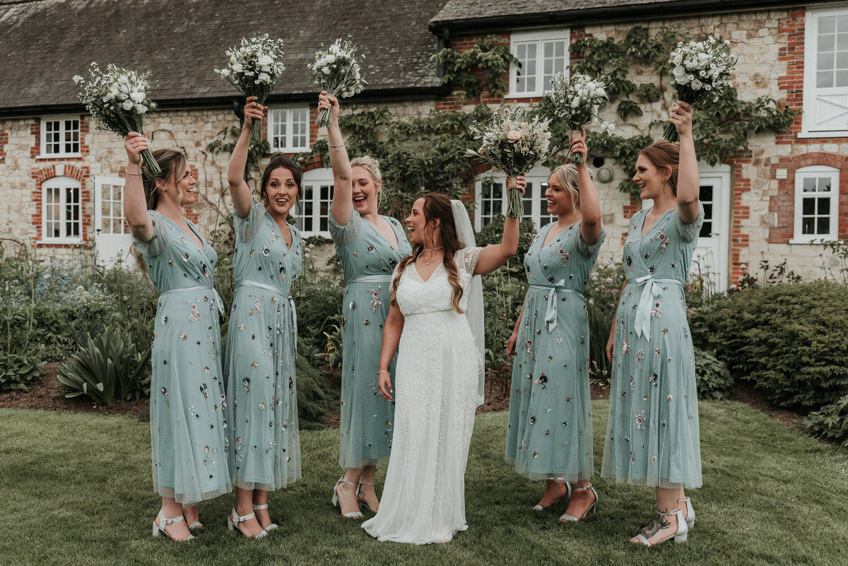 Bridesmaids in beautiful embroidered sage green dresses celebrate with their bride at a fun spring wedding at Bury Court Barn, Farnham