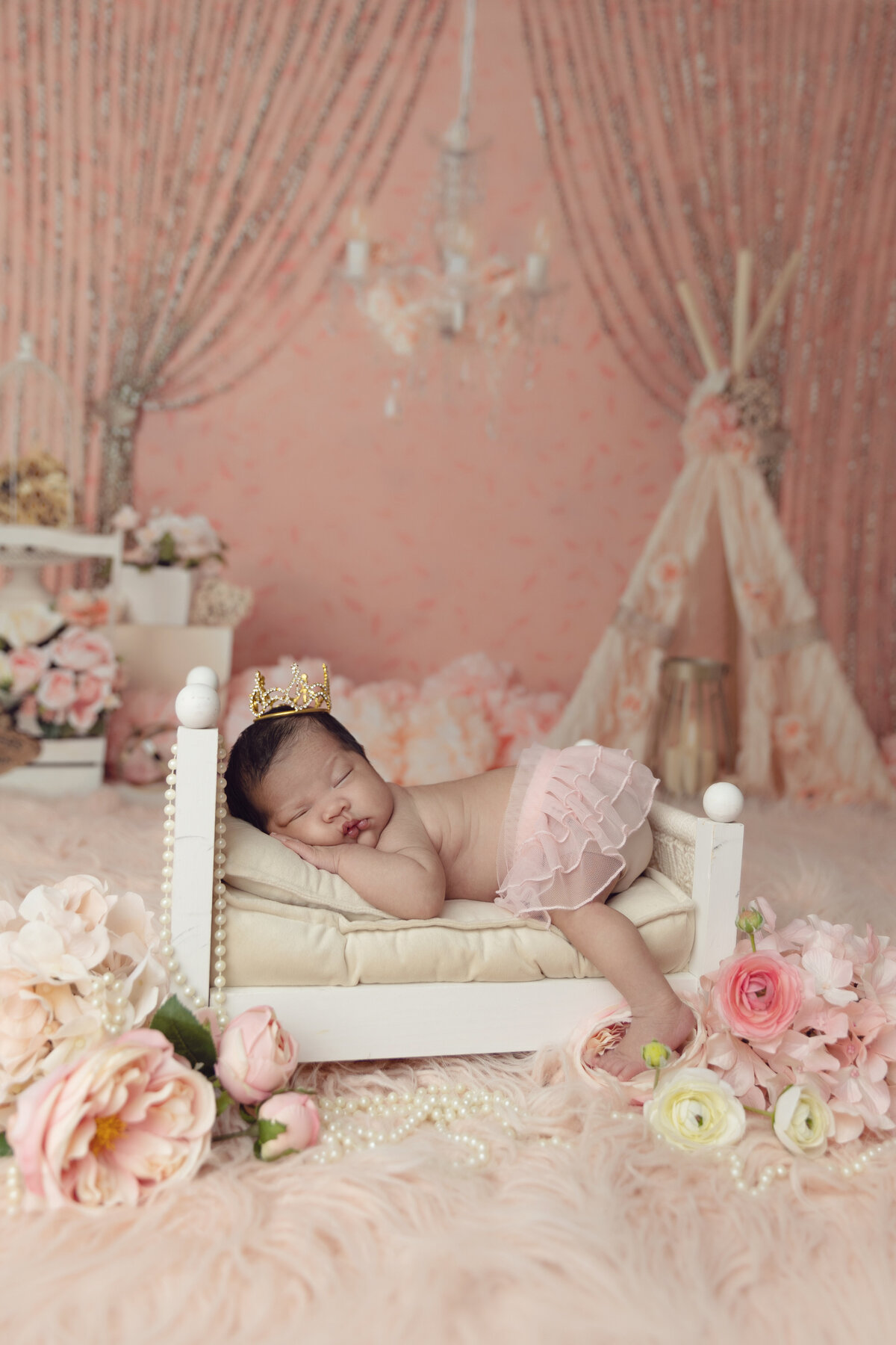 A sleeping newborn baby girl lays on her hands in a tiny white bed in a pink tutu