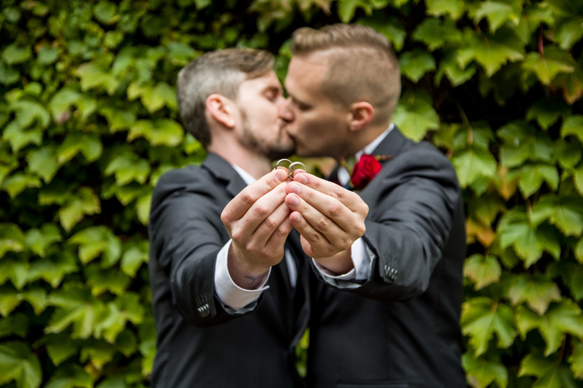 Grooms kiss while holding rings.