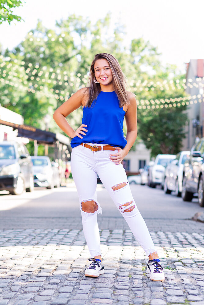 High school photography session of a senior girl wearing white jeans standing on a cobble stone street in downtown Raleigh, NC.