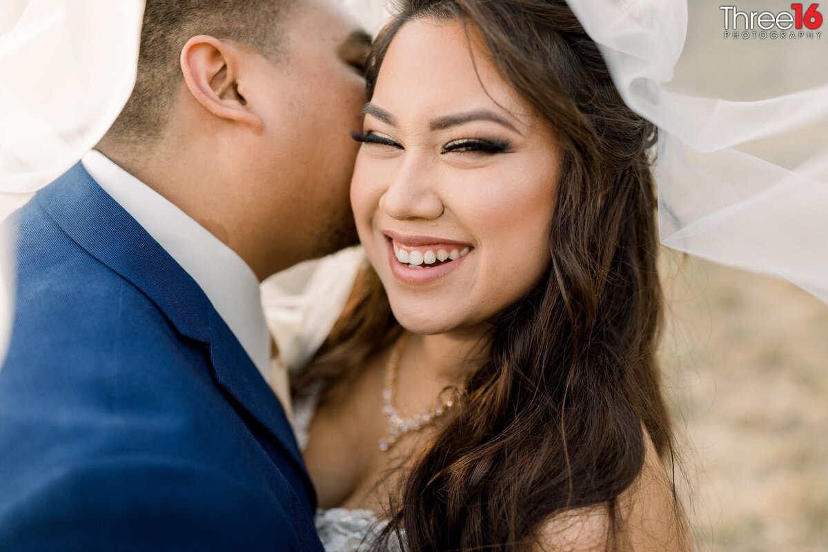 Bride shares a big smile while her Groom kisses her cheek