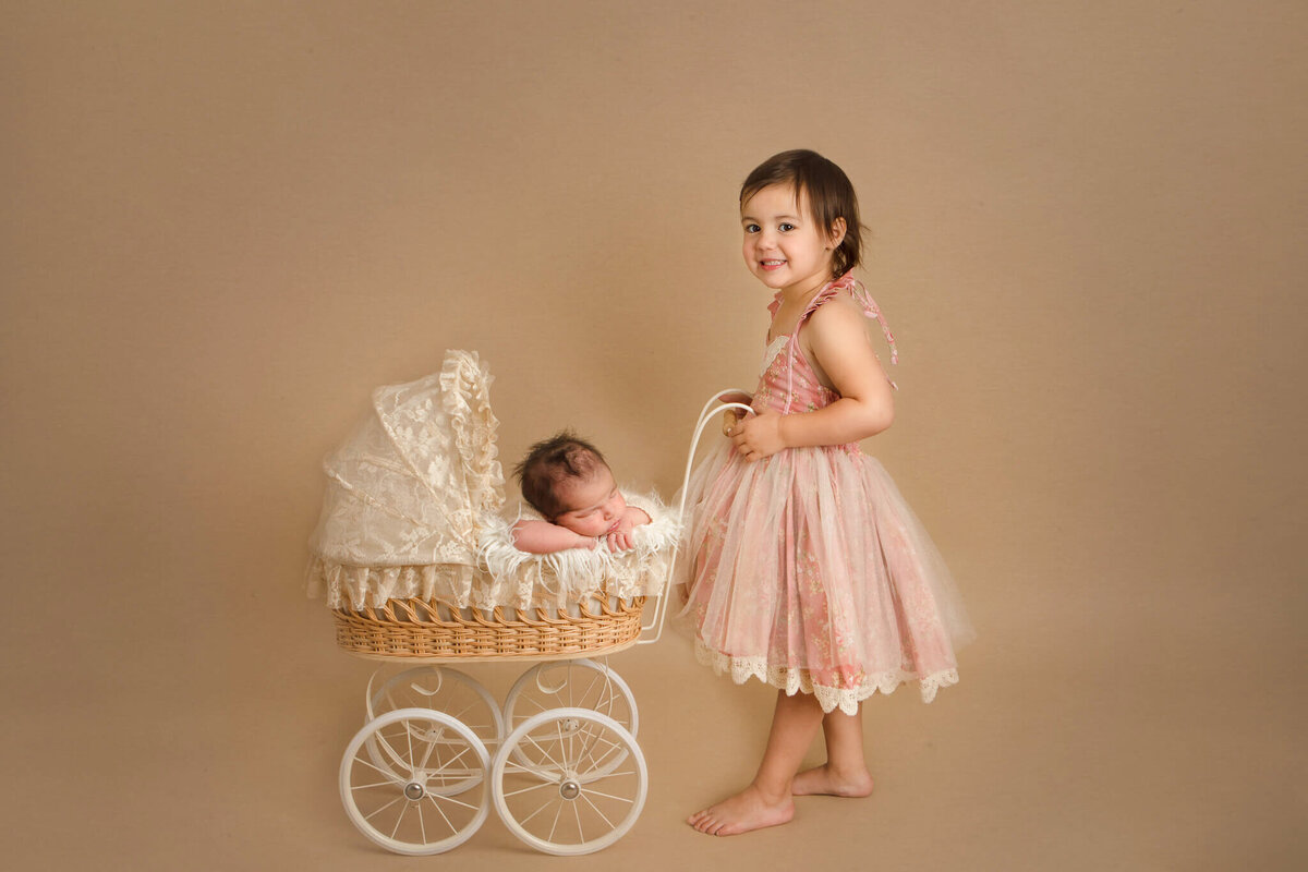 Older sister with newborn baby sister in an old fashioned stroller photographed by Woodland Hills newborn photographer