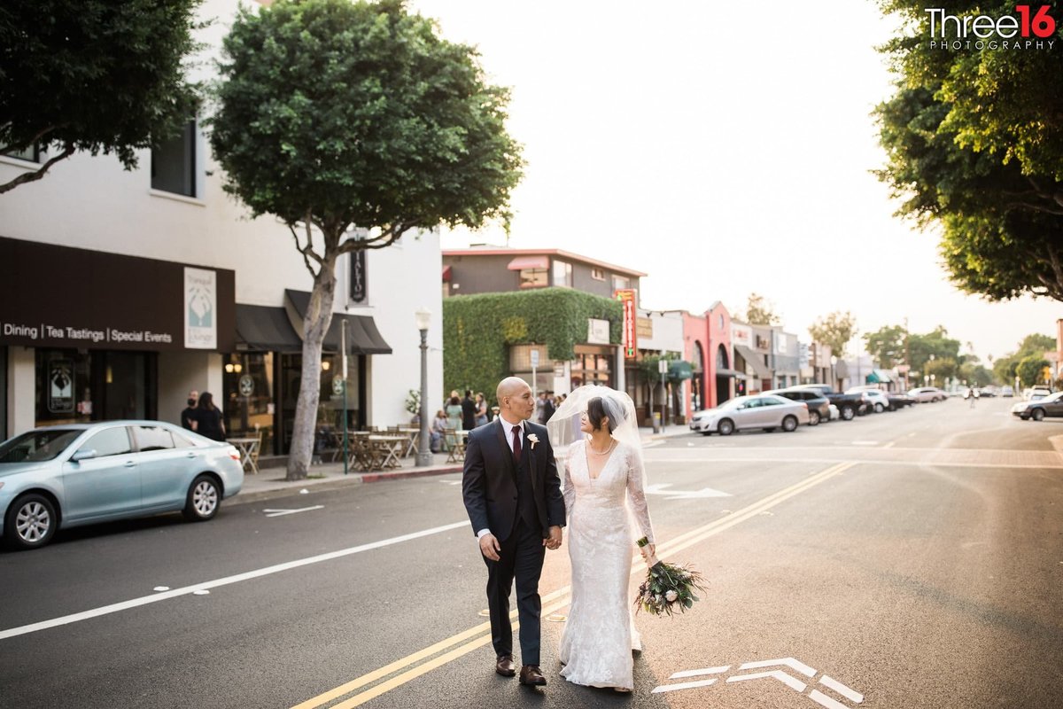Bride and Groom look at each other as they walk across the street while holding hands