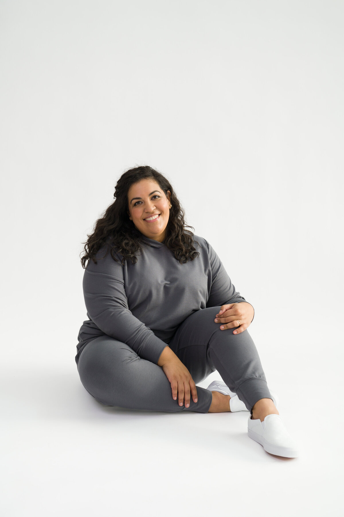 Woman sitting on floor with white background wearing grey joggers