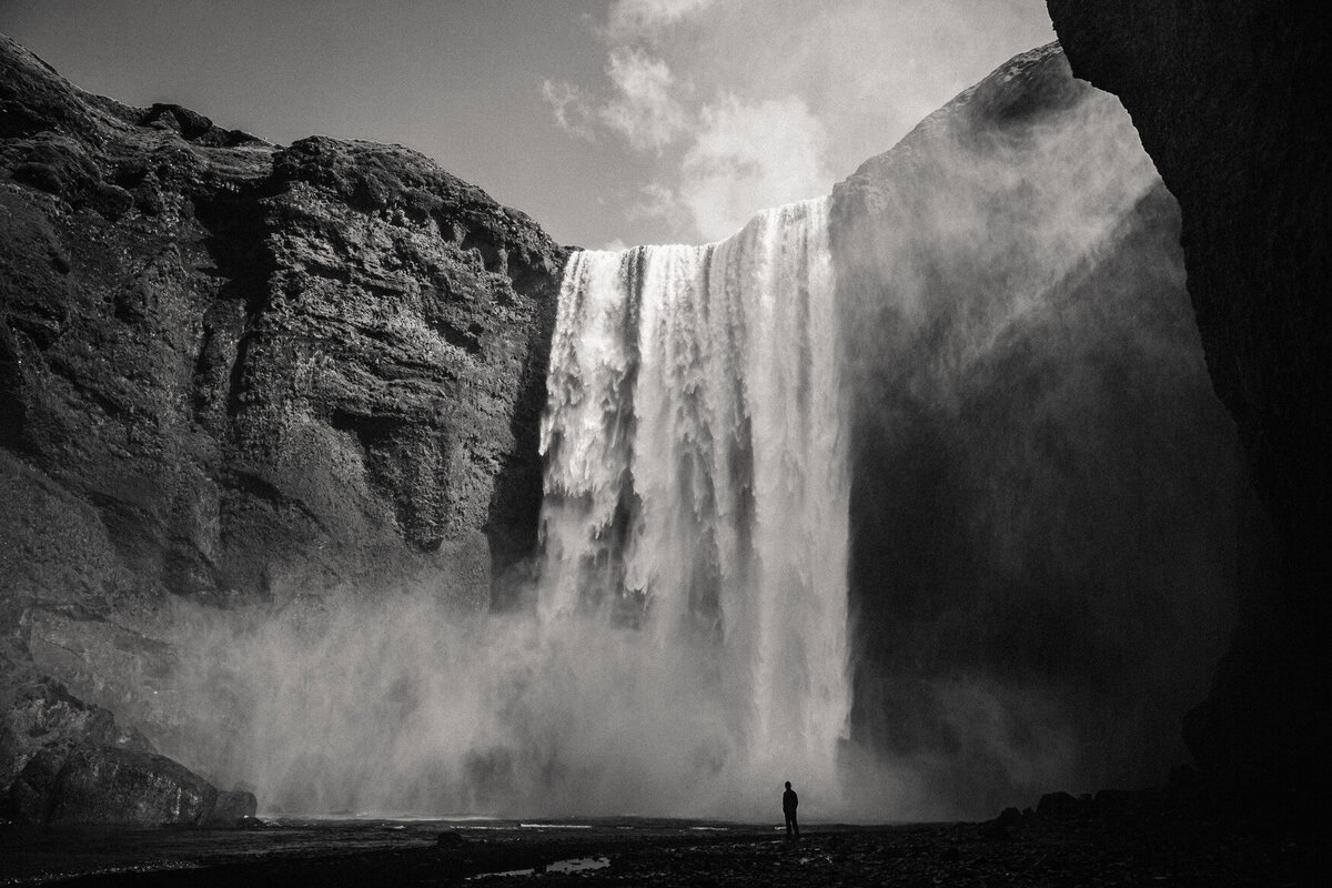 Environmental portrait of man in front of Skogafoss waterfall in icealand