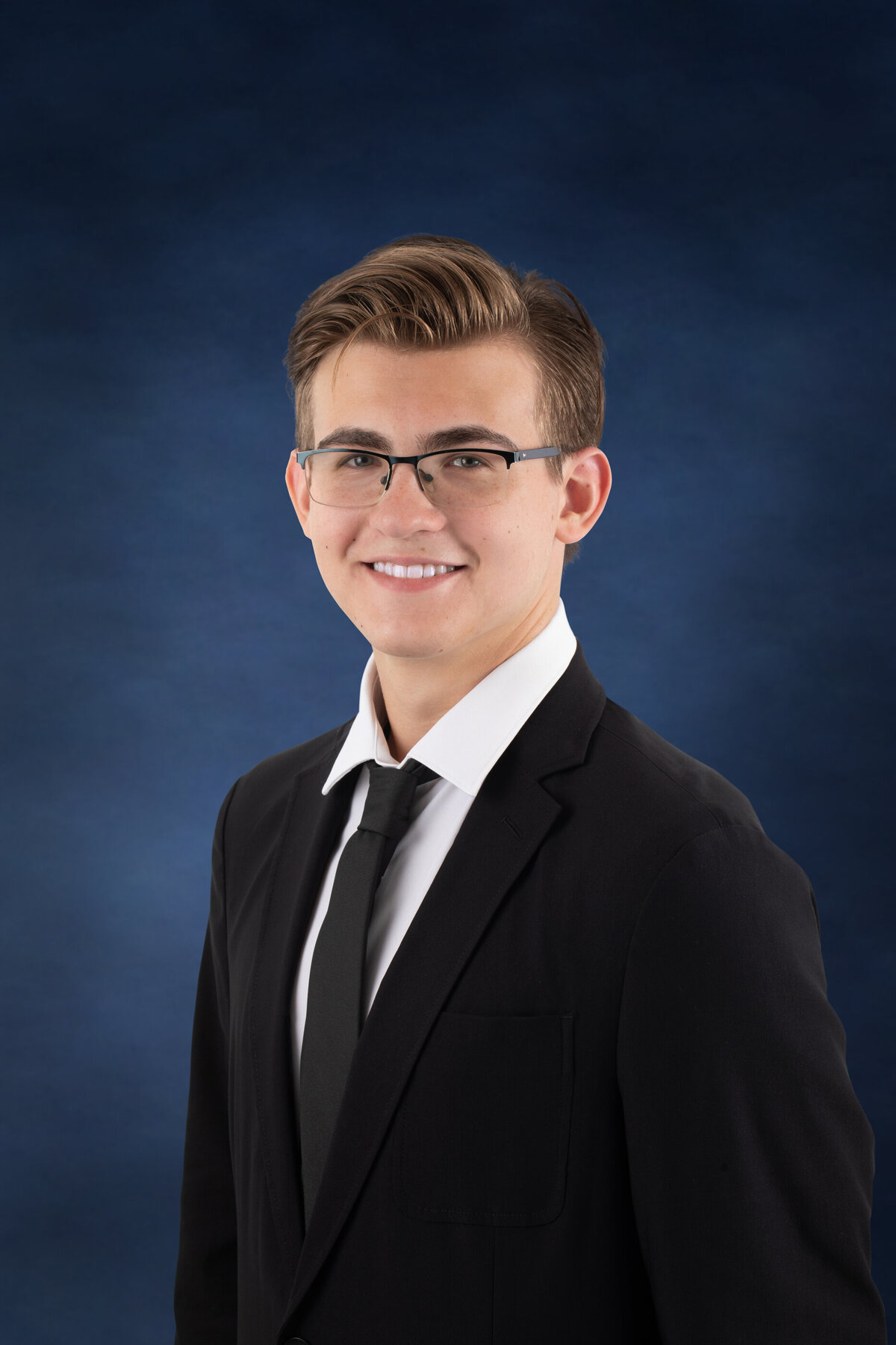 A teenage boy with blond hair and classes wears a black suit and tie for yearbook photo Clarsktown North senior portrait photographer Milestone Images