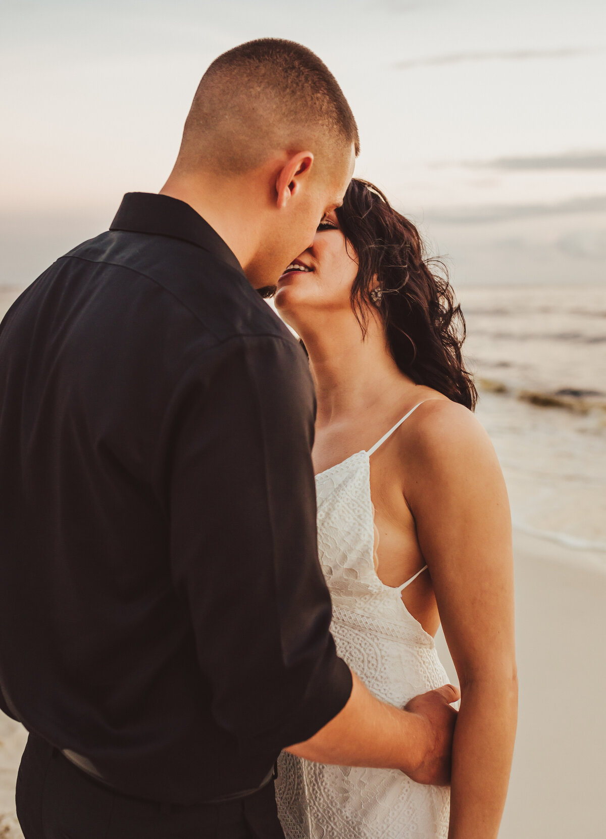 newlyweds kiss at sunset, he's wearing all black, she's wearing white wedding dress.  Taken by panama city wedding photographer Brittney Stanley