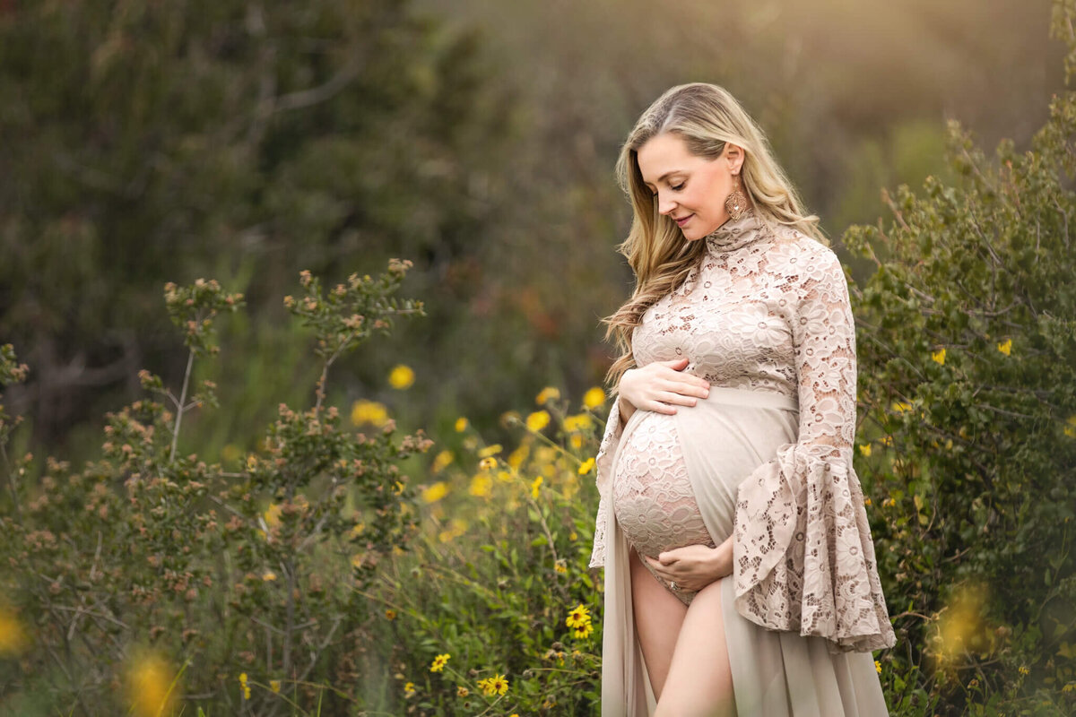 New mom to be looking at her baby bump in a Los Angeles park wearing a beige Mii Estilo Dress
