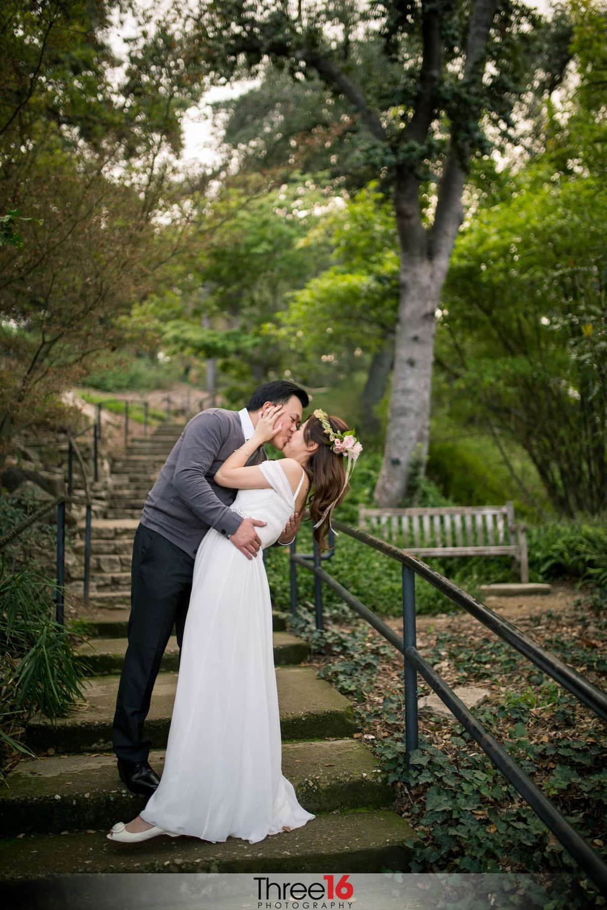 Groom leans in and kisses his Bride on the stairs at the LA Arboretum
