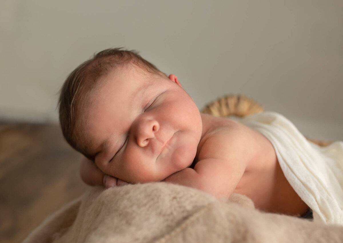 A newborn baby boy sleeps with his arms folded under his cheek