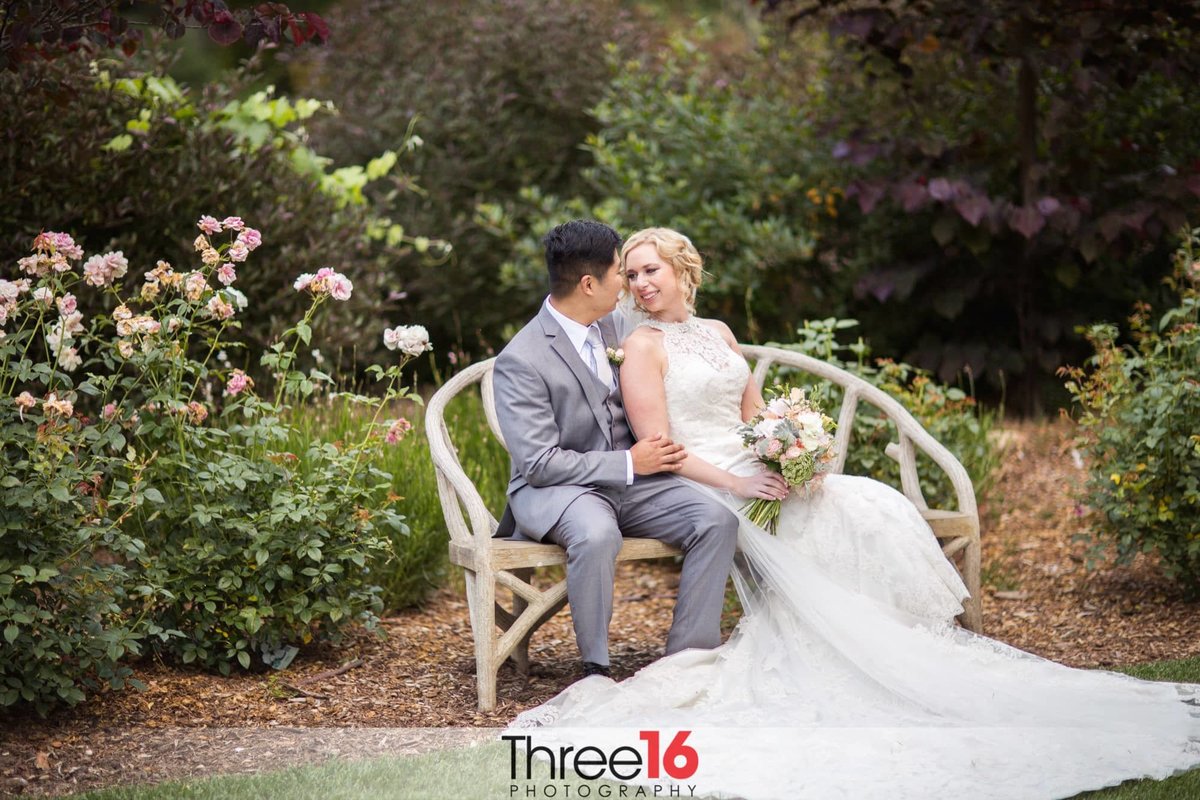 Bride cozies up to her Groom as they sit on a garden bench together