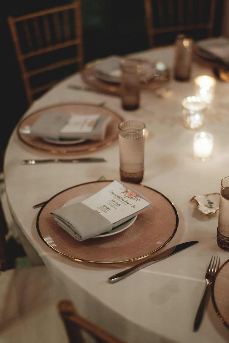 Floral wedding menus tucked in napkins sit atop blush and gold plates at romantic Fort Lauderdale reception