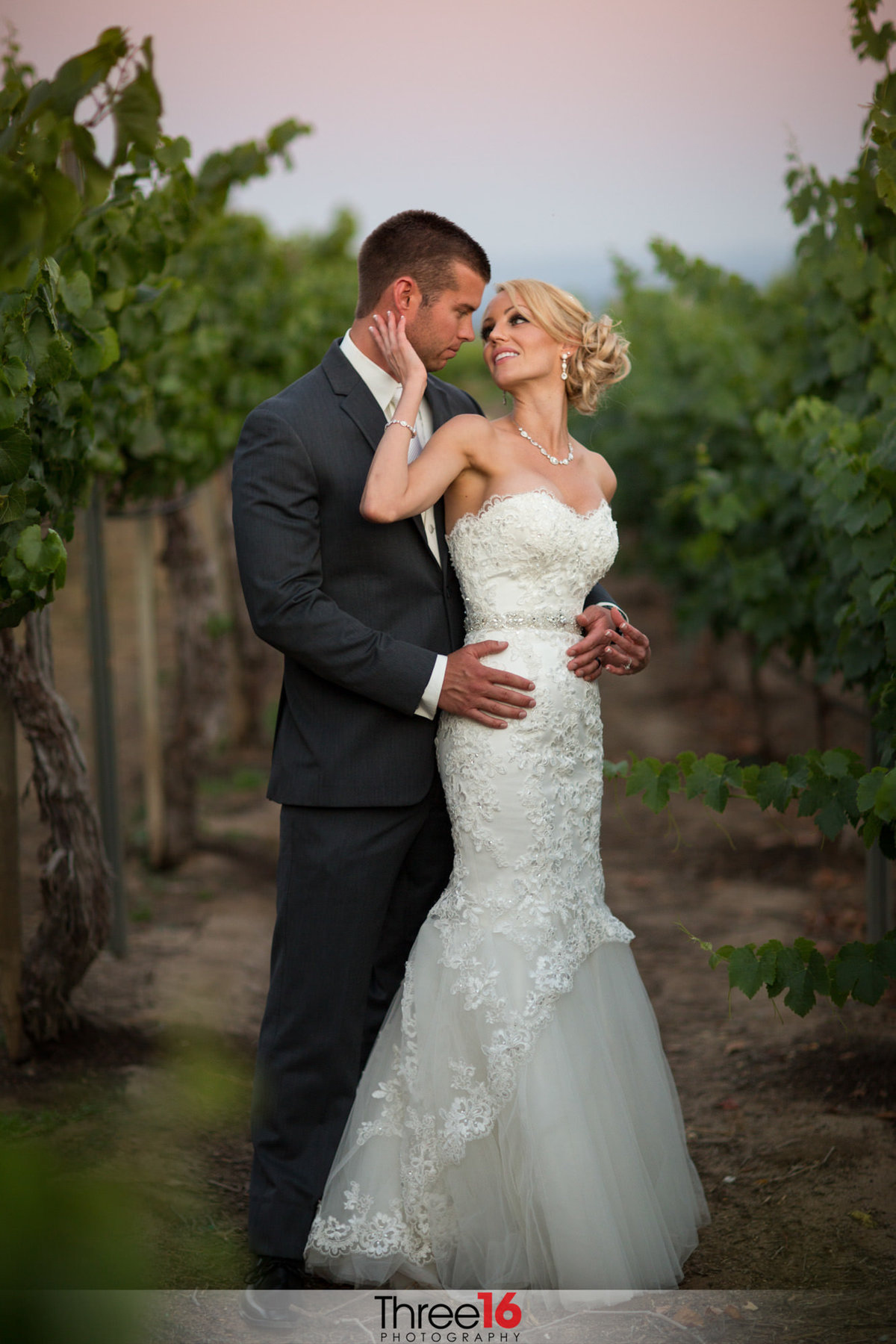 Bride looks back at her Groom as they gaze into each other's eyes while standing in a winery orchard