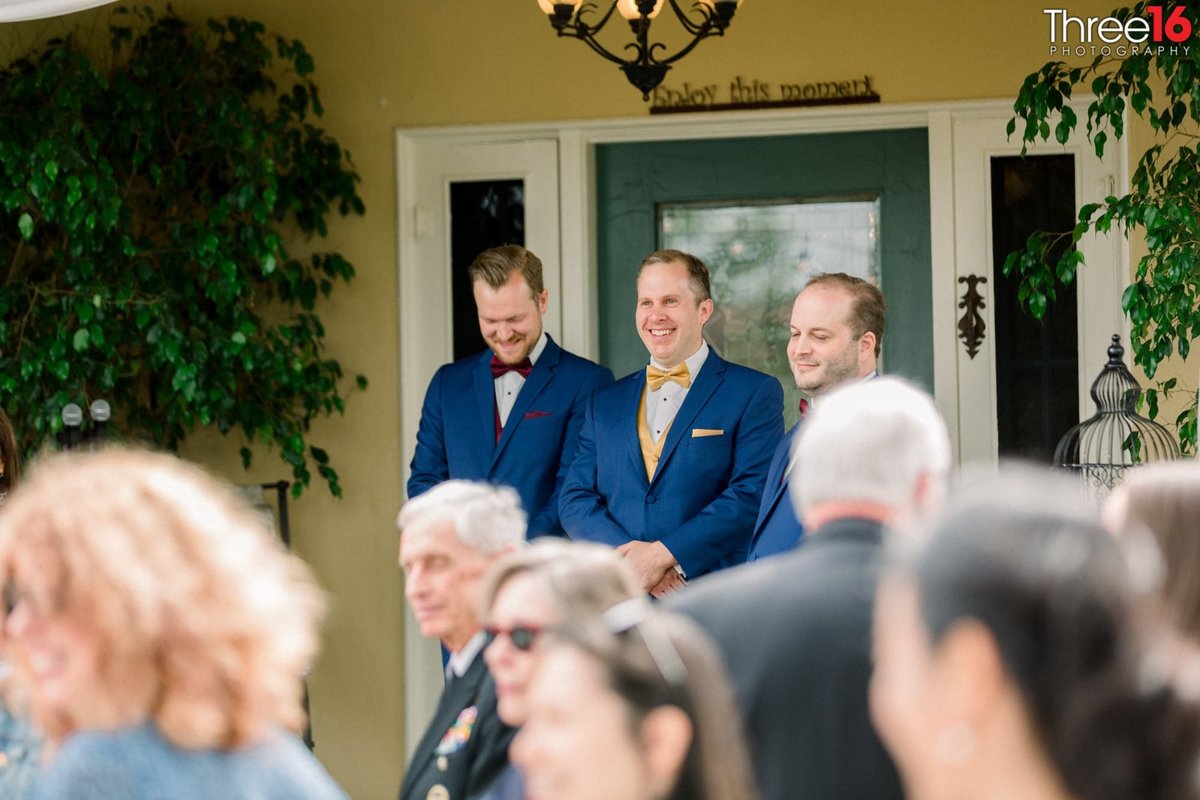 Groom and Groomsmen stand at the aisle smiling as Bride approaches