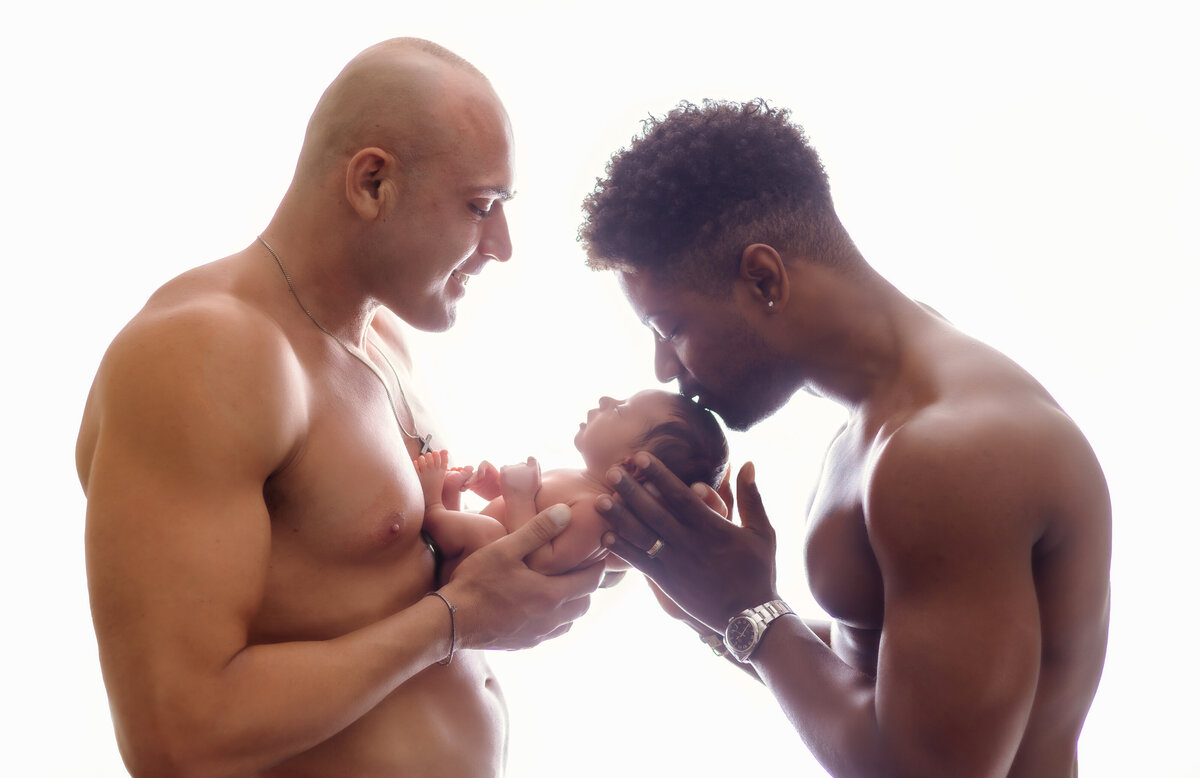 Newborn Photographer, two men stand together shirtless, they holds their baby
