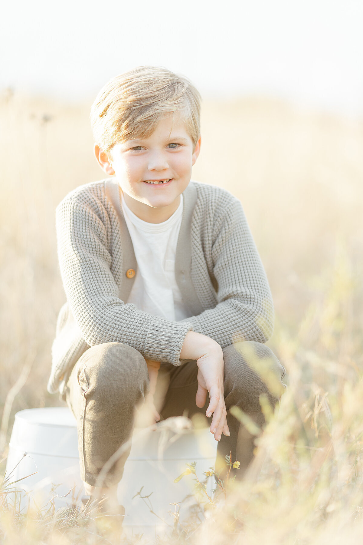Portrait of a young boy sitting on a bucket in the middle of a Fort Worth park as he smiles for his family pictures.