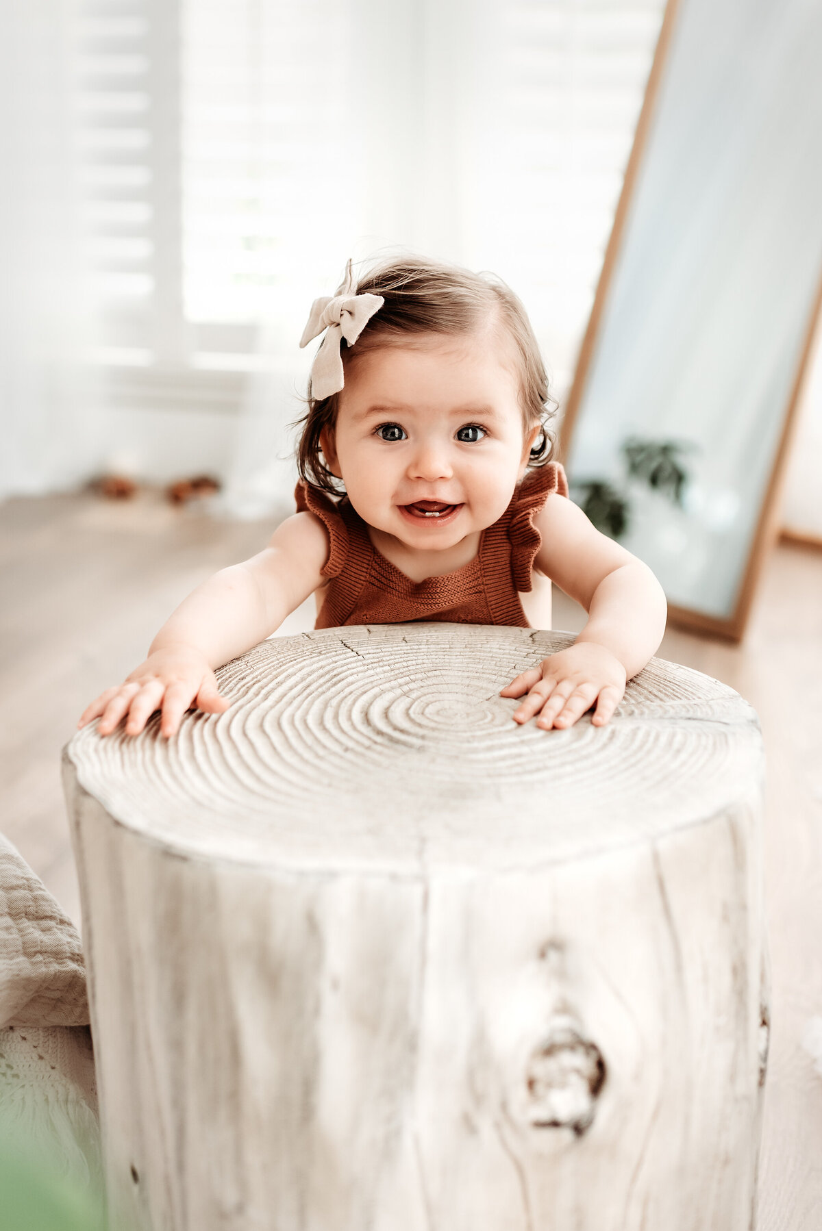 baby girl standing near tree stump prop in photo studio