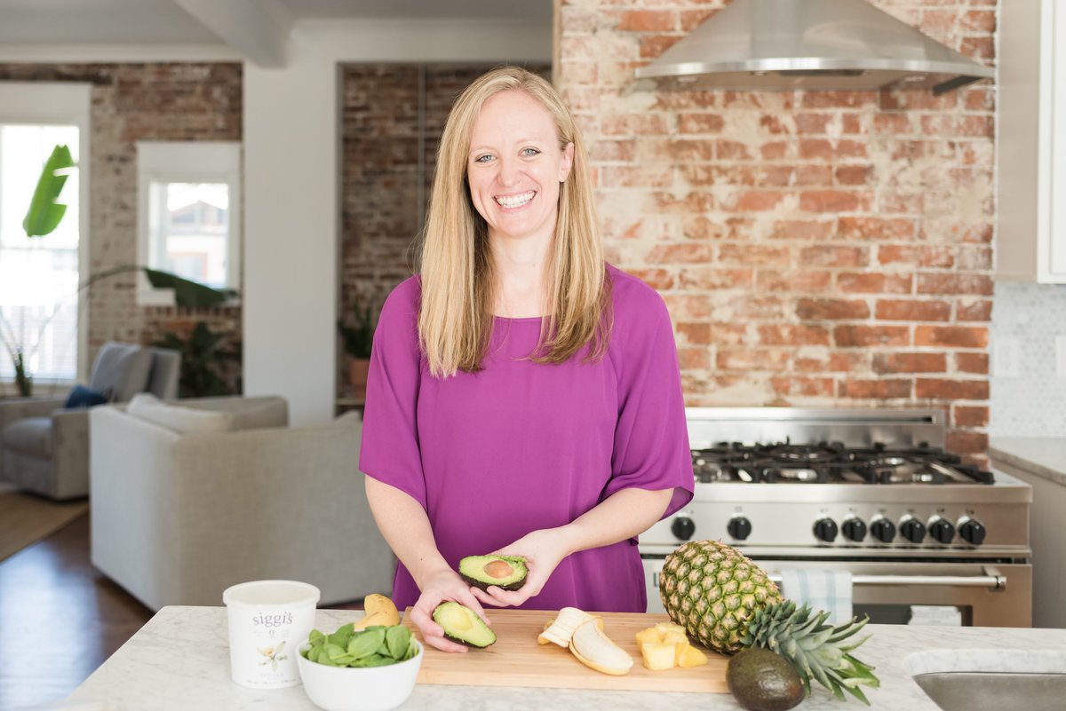 Nashville nutritionist in a kitchen holding avocados with other fruits around her