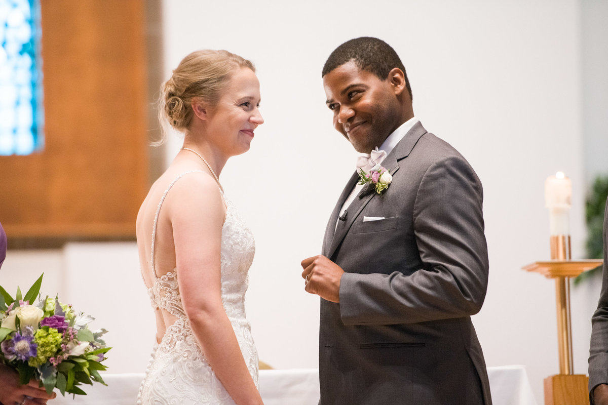 Black groom and bride laugh during church wedding ceremony.