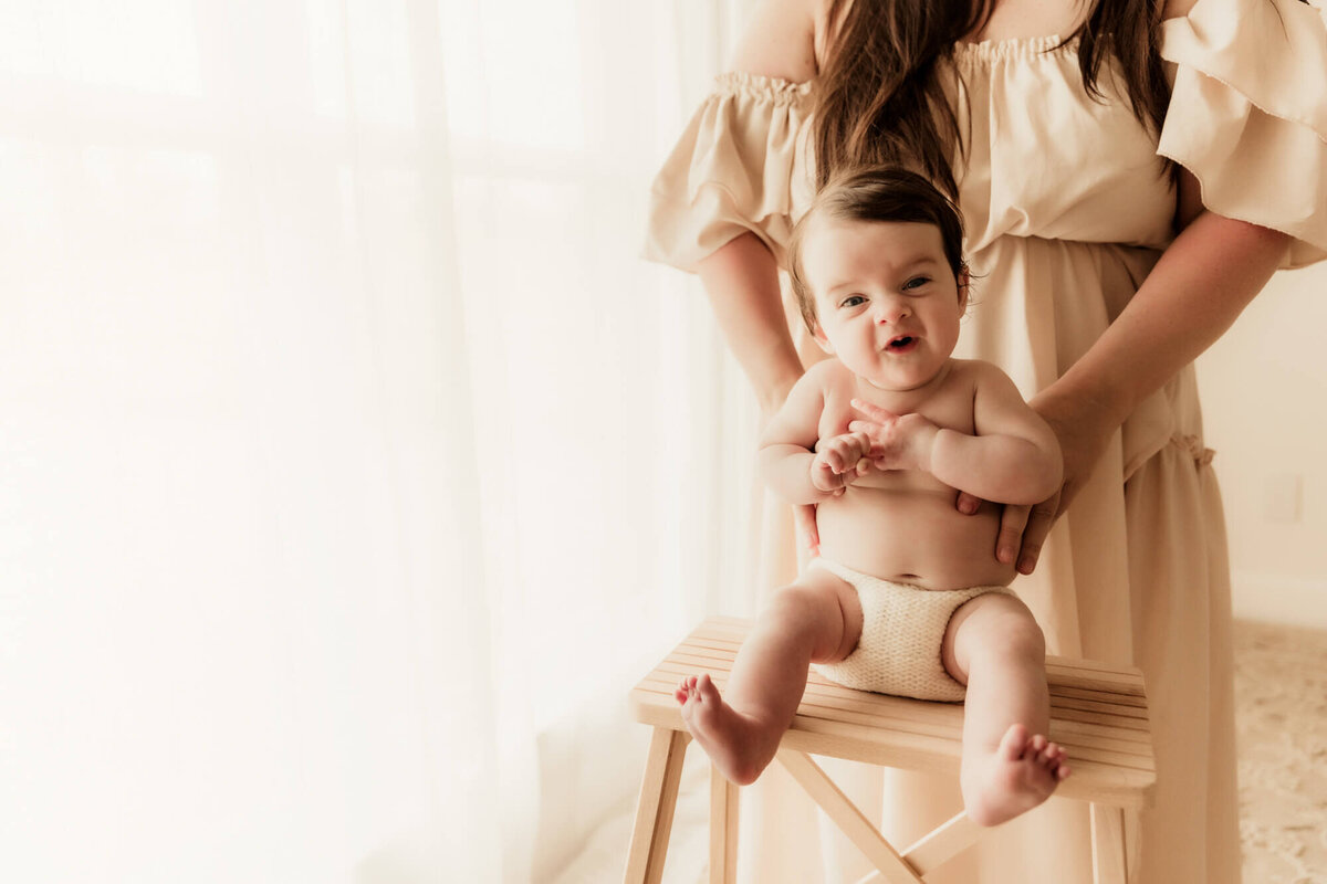 Baby girl sitting on a stool with and excited expression.